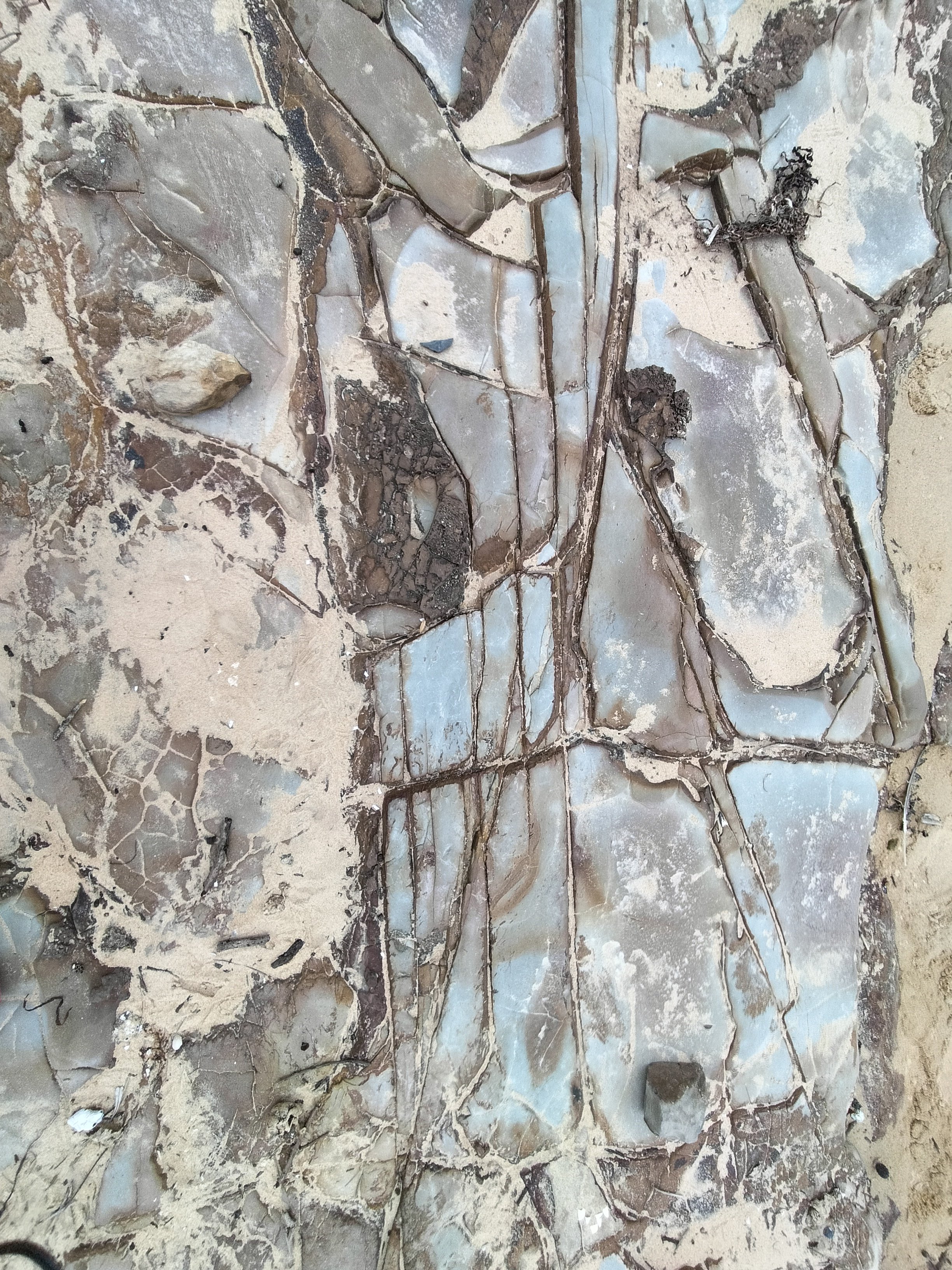 Close-up view of a mosaic wall made from irregularly shaped pieces of marble and stone, with some dirt and debris present.