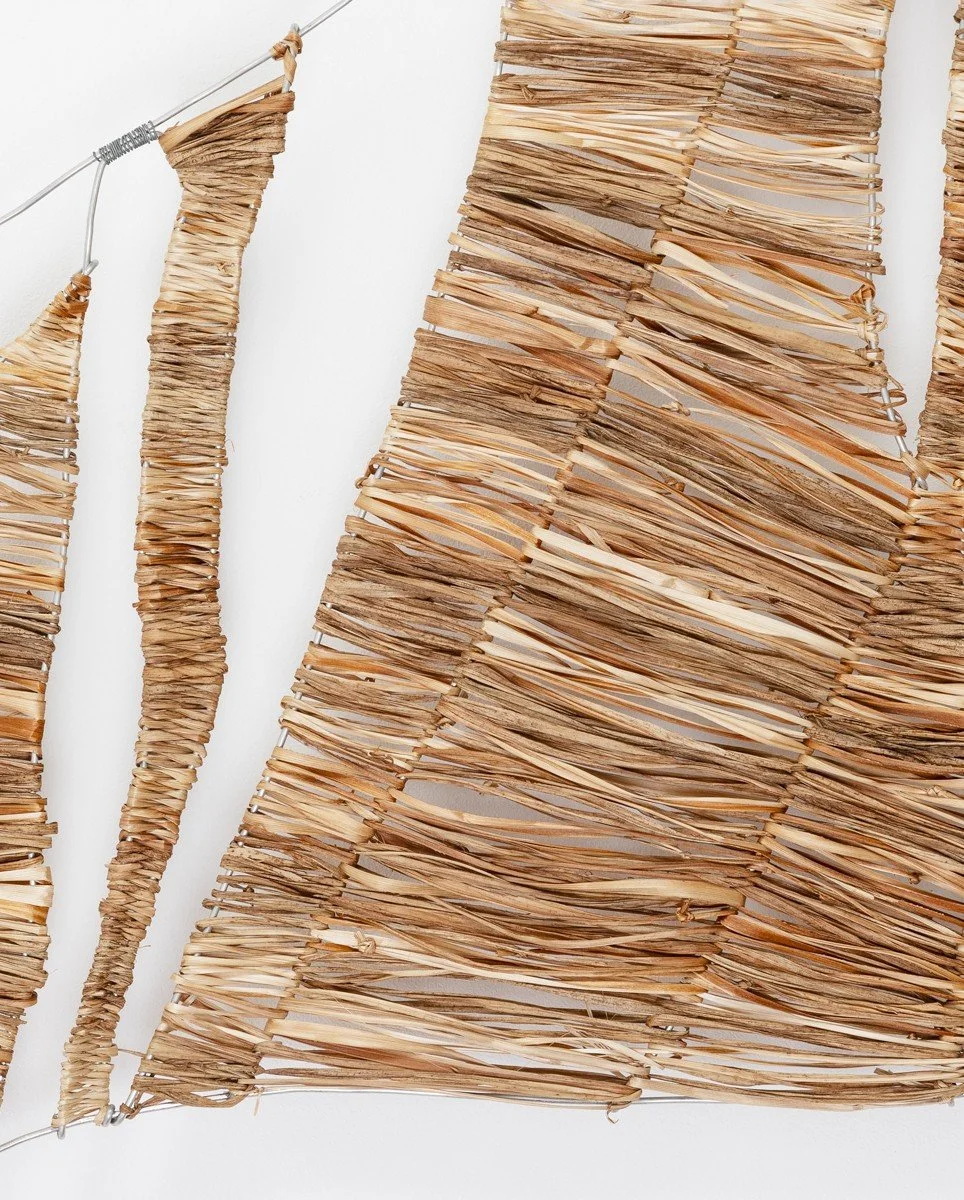 Close-up of a decorative art piece made from layered and twisted dried palm leaves or similar natural fibers, mounted on a wall.