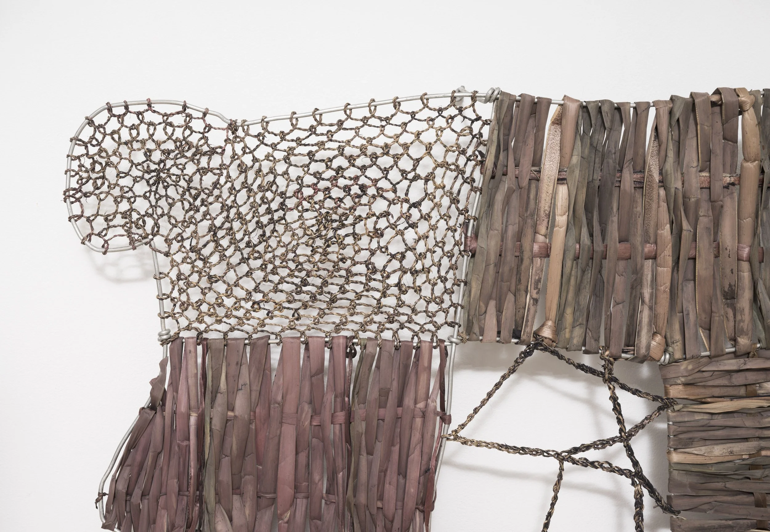Close-up of a sculpture made from wood, metal, and rope, featuring woven and assembled materials on a white background.