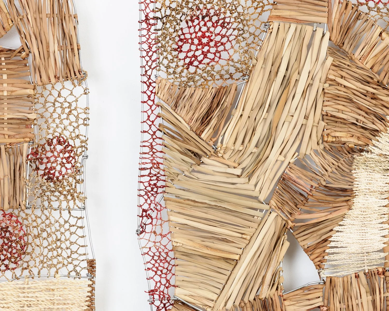 Close-up view of a textured wall art installation made from woven natural materials, such as wood and straw, with different patterns and colors, mounted on a plain white wall.