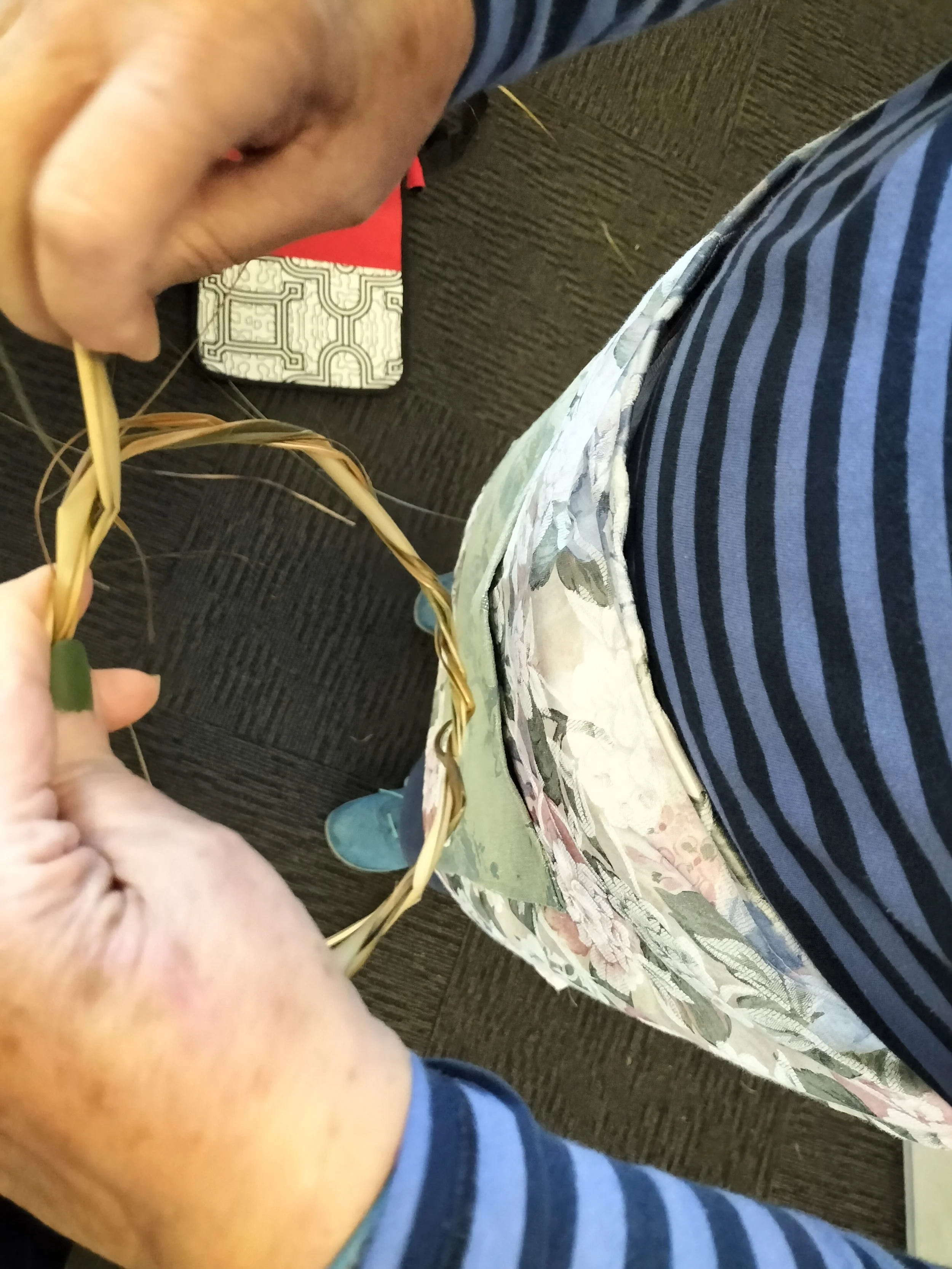 A person holding a small ring of natural fibres to start a basket, while standing wearing a floral patterned apron.