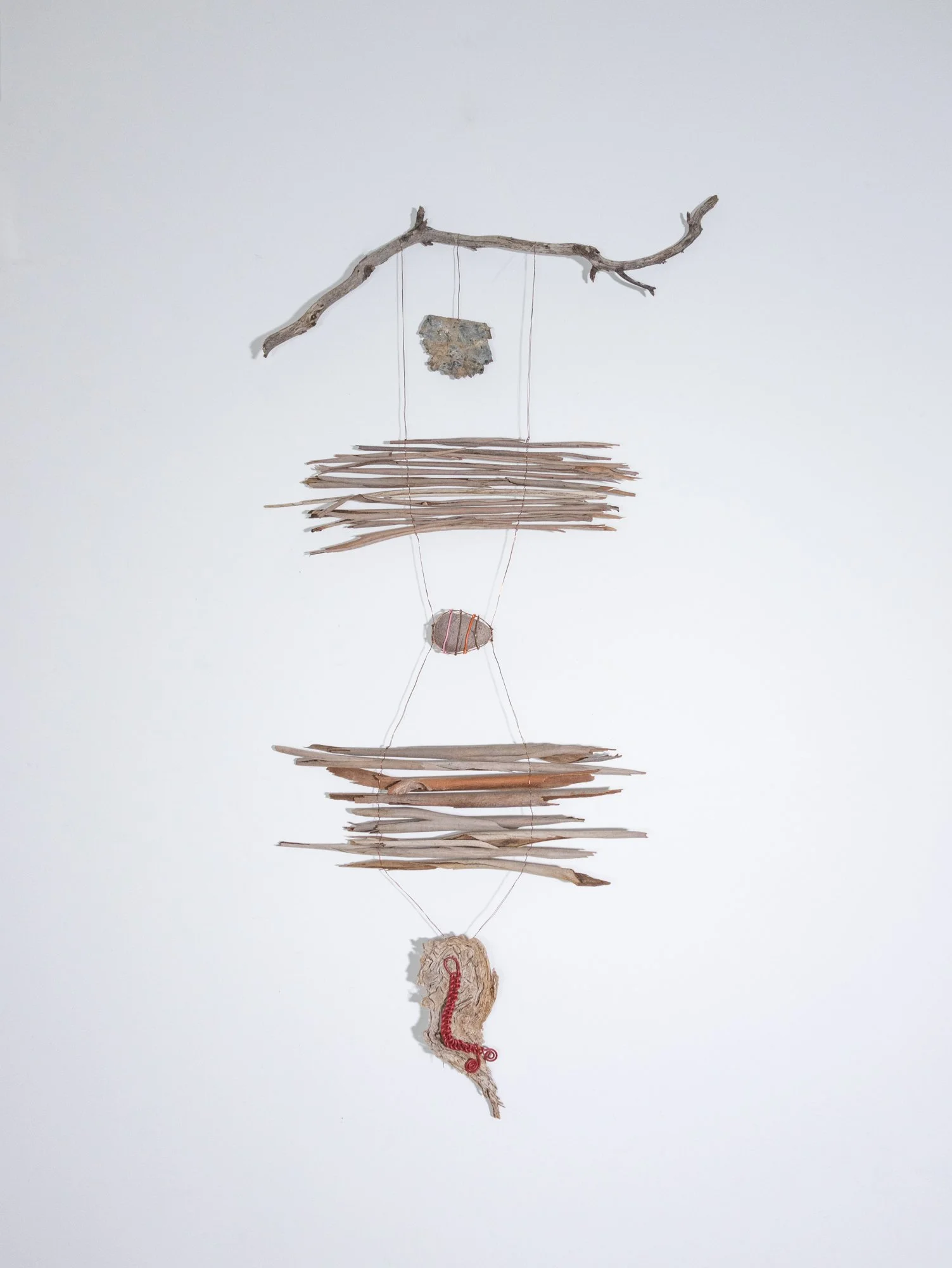 A hanging art installation made of eucalyptus bark, string, wire, and a rock.