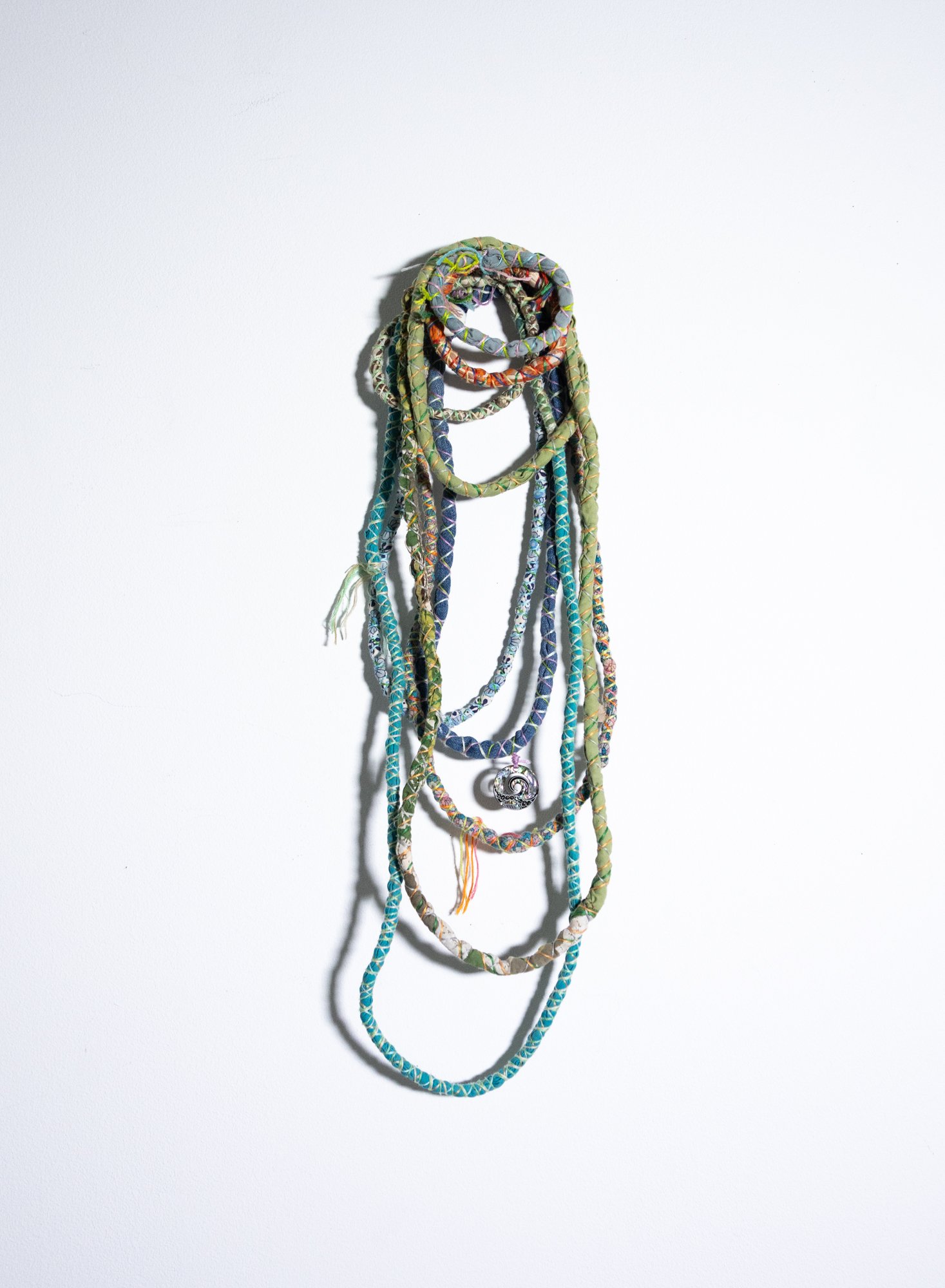 Colorful, braided necklaces hanging against a white wall.