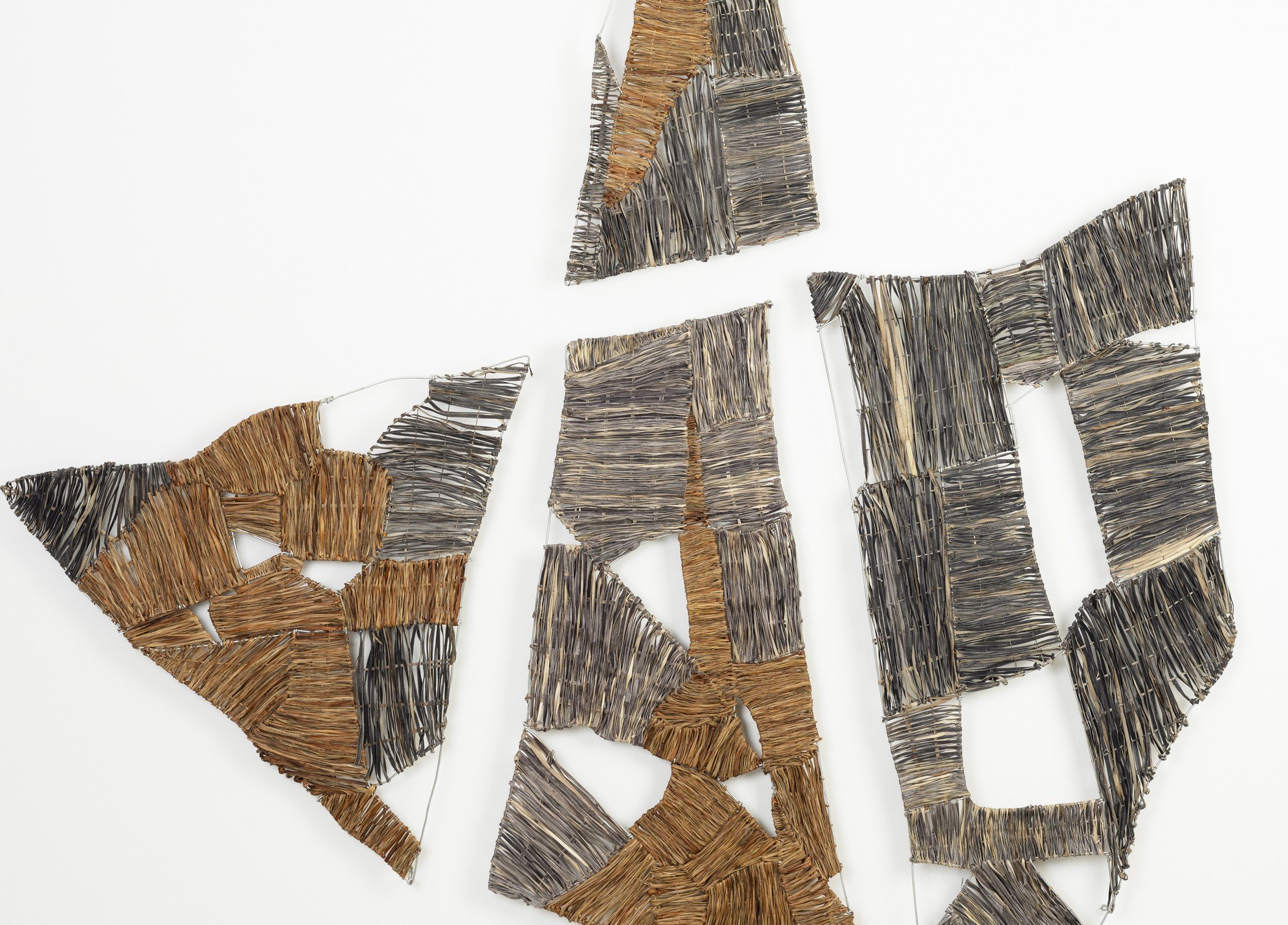 Close-up of an art installation made from various shades of brown and gray wooden sticks assembled on a white background.