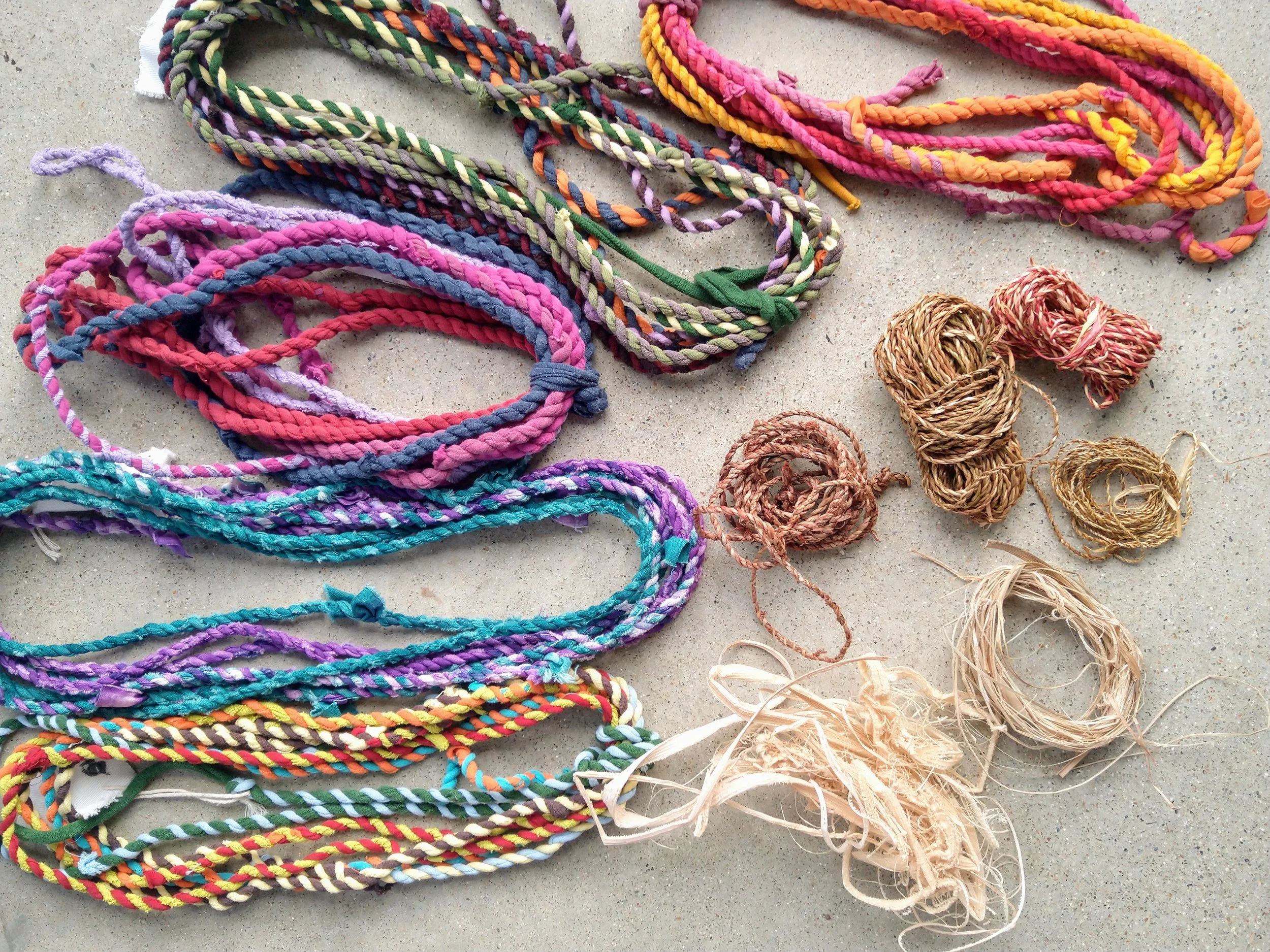 Colourful twined cotton ropes and coils of natural fibre string on a concrete surface.