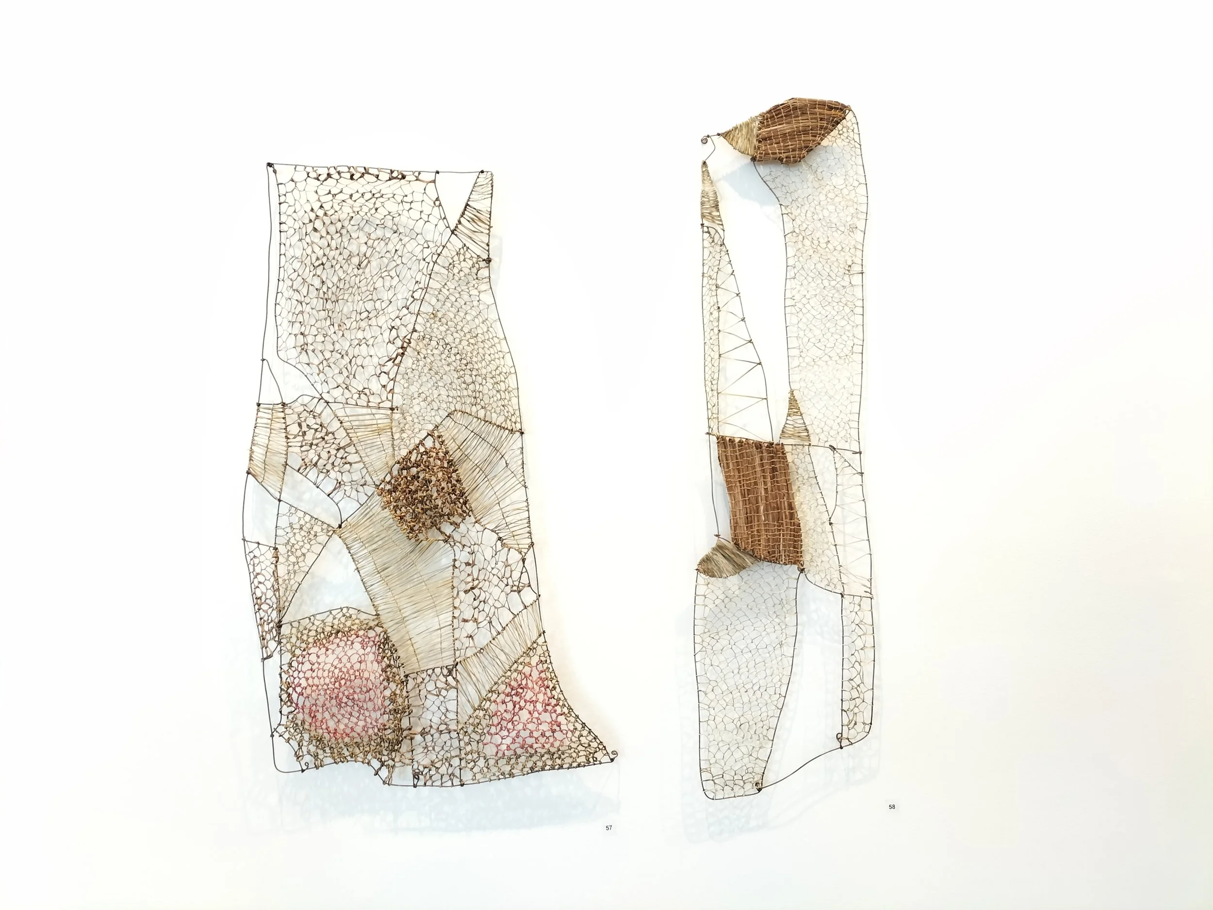 Two contemporary art sculptures made of woven wire and metallic materials, mounted on a white wall.