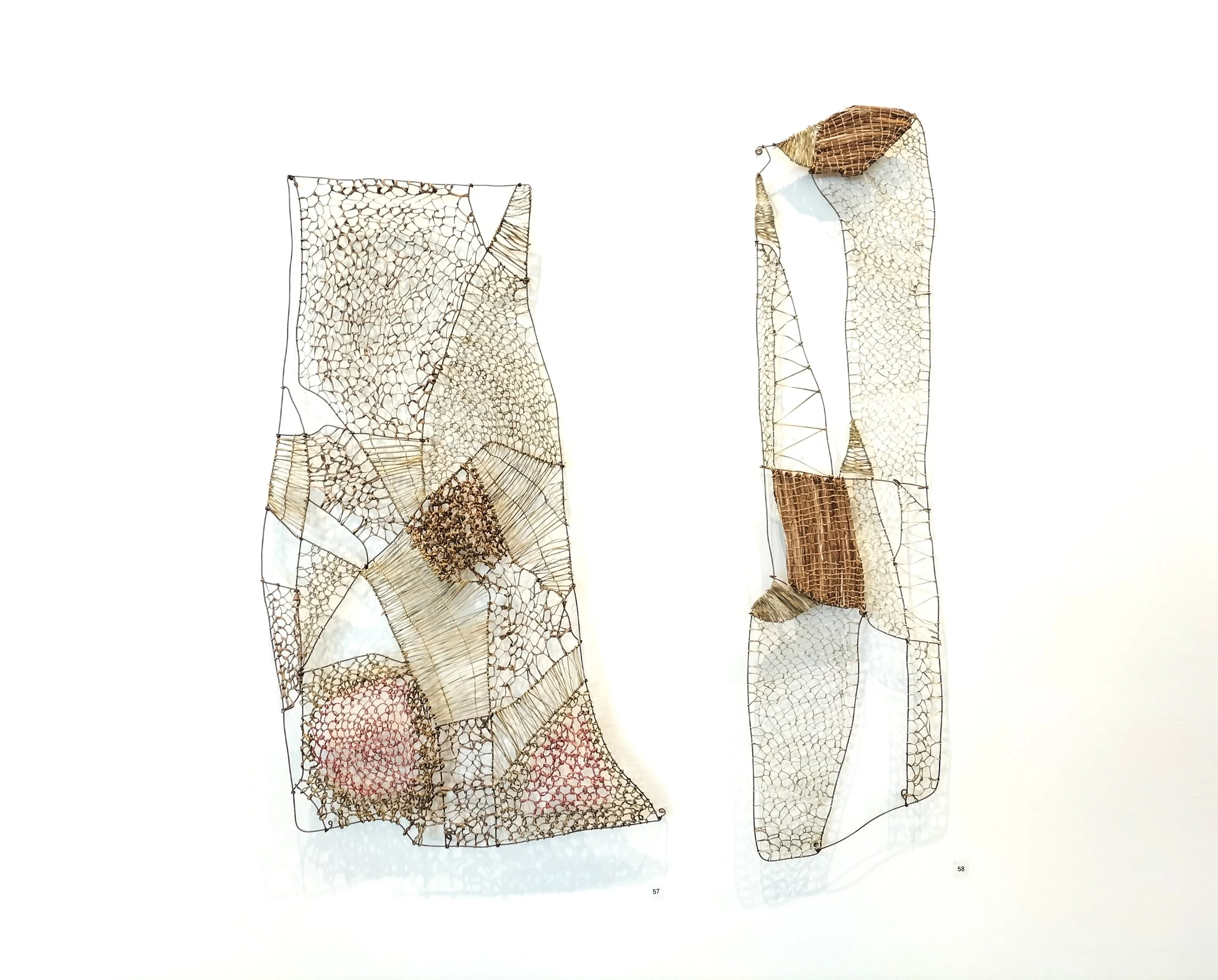 Two tall, abstract sculptures made of woven and wire materials, resembling elongated human figures with exposed skeletal structures and textured surfaces.