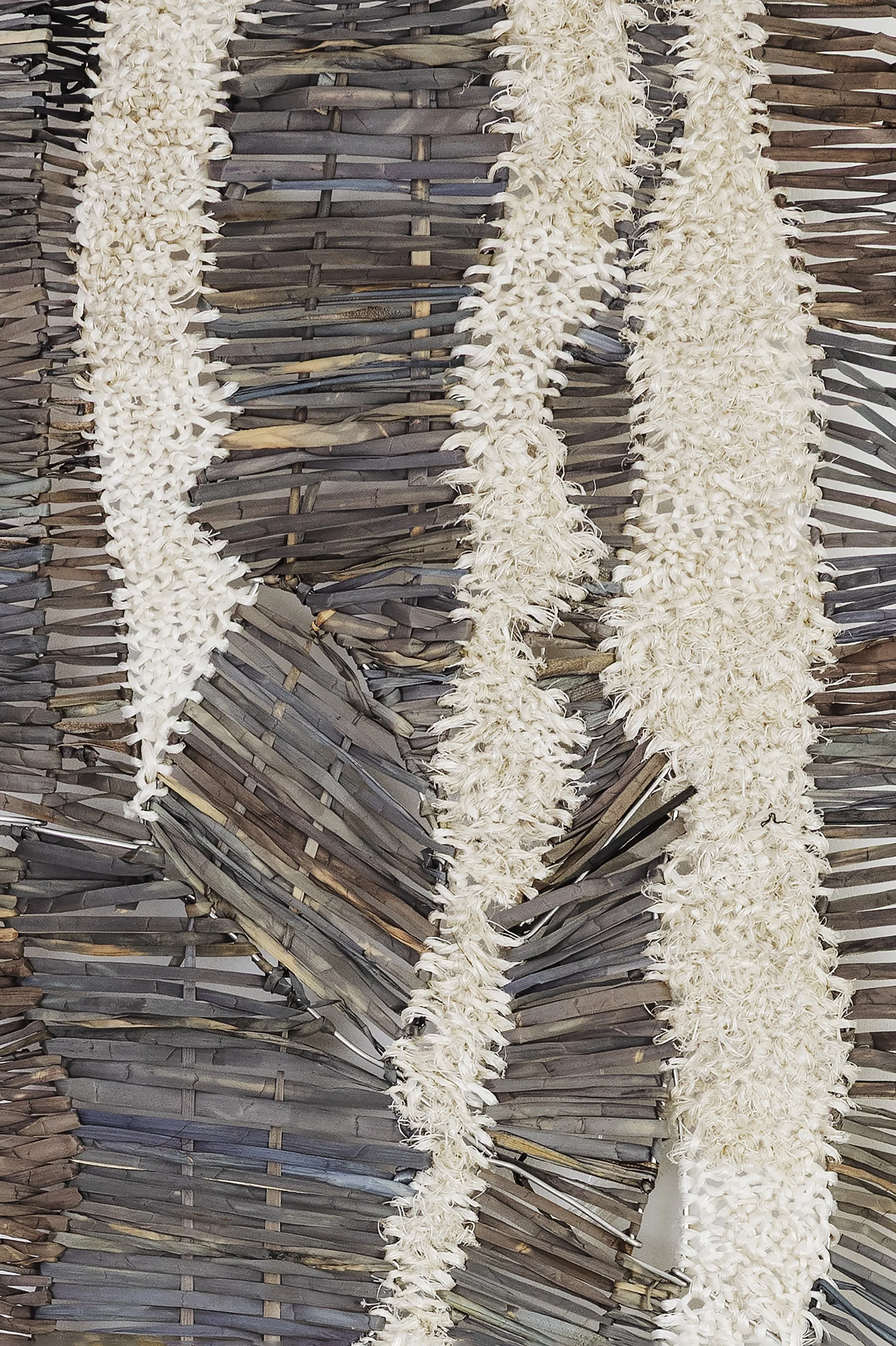 Close-up of a textured woven surface made from palm or bamboo leaves, with several white flower garlands hanging vertically across it.