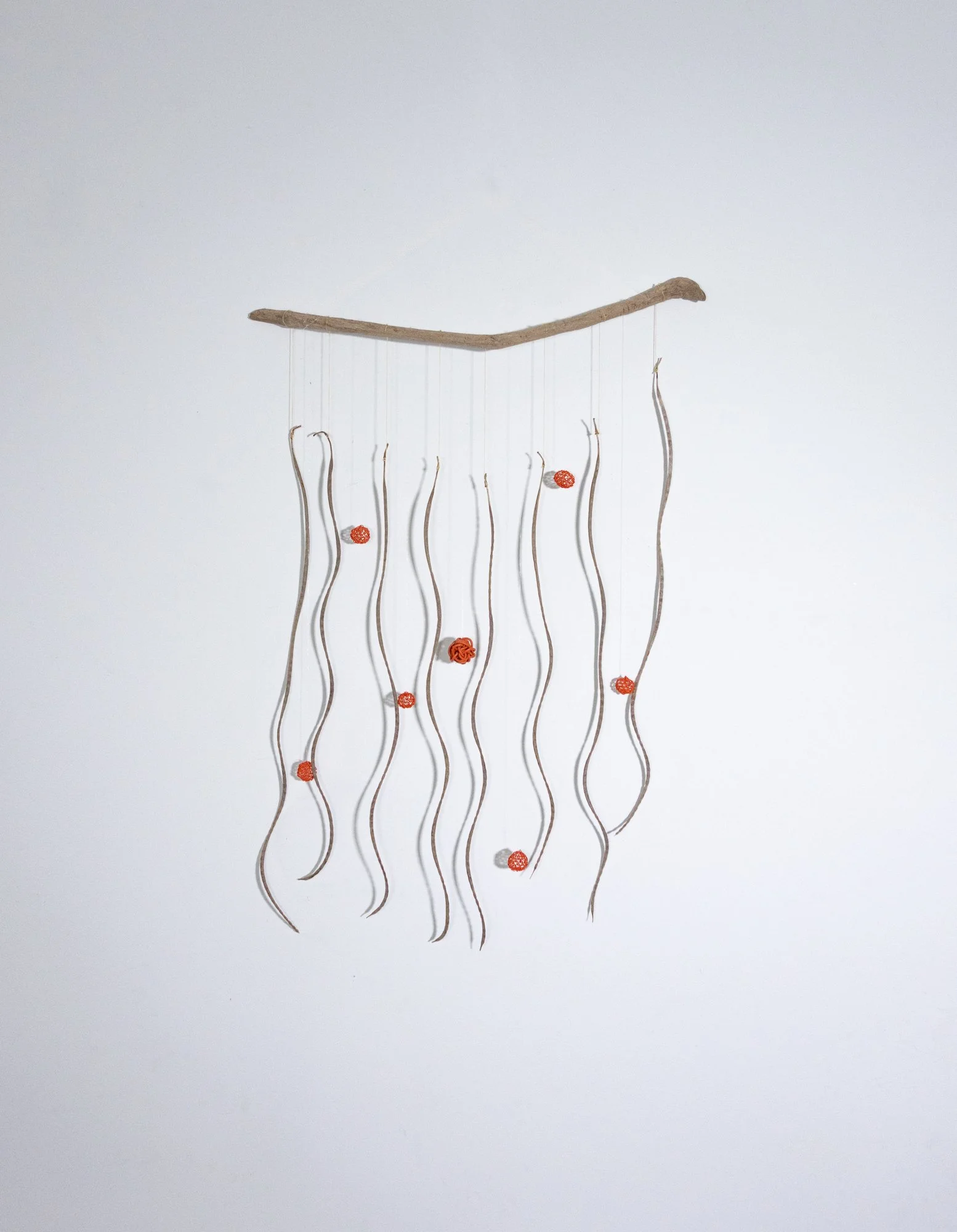 A yarn mobile with seven seed pods hanging from a brown stick, with small red wire balls attached to the strings.