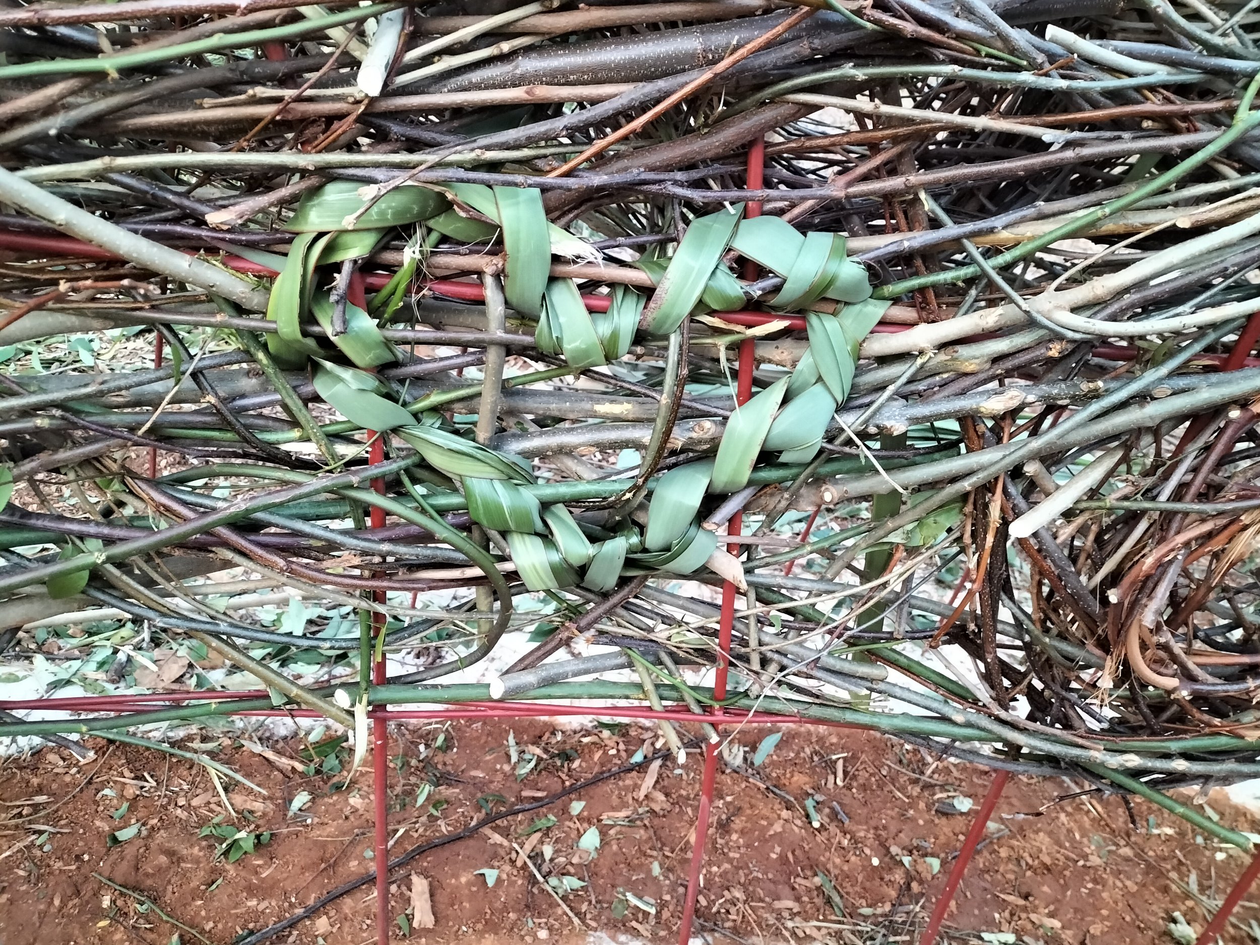 A structure made of branches and twigs entwined with green leaves shaping a heart.