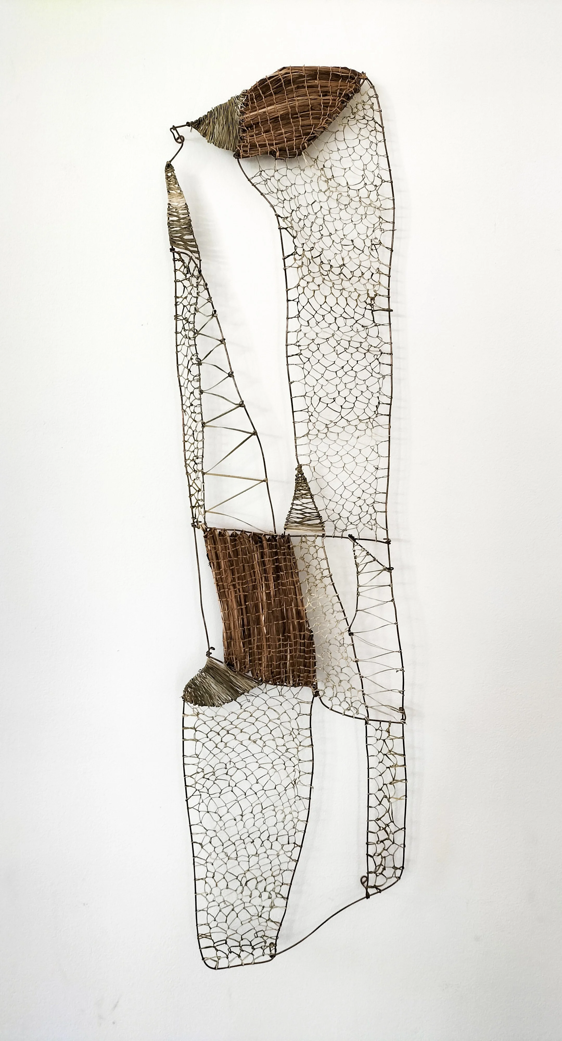 A mixed-media wall sculpture made of wire, wood, and fabric, designed in an abstract, elongated shape with textured sections.