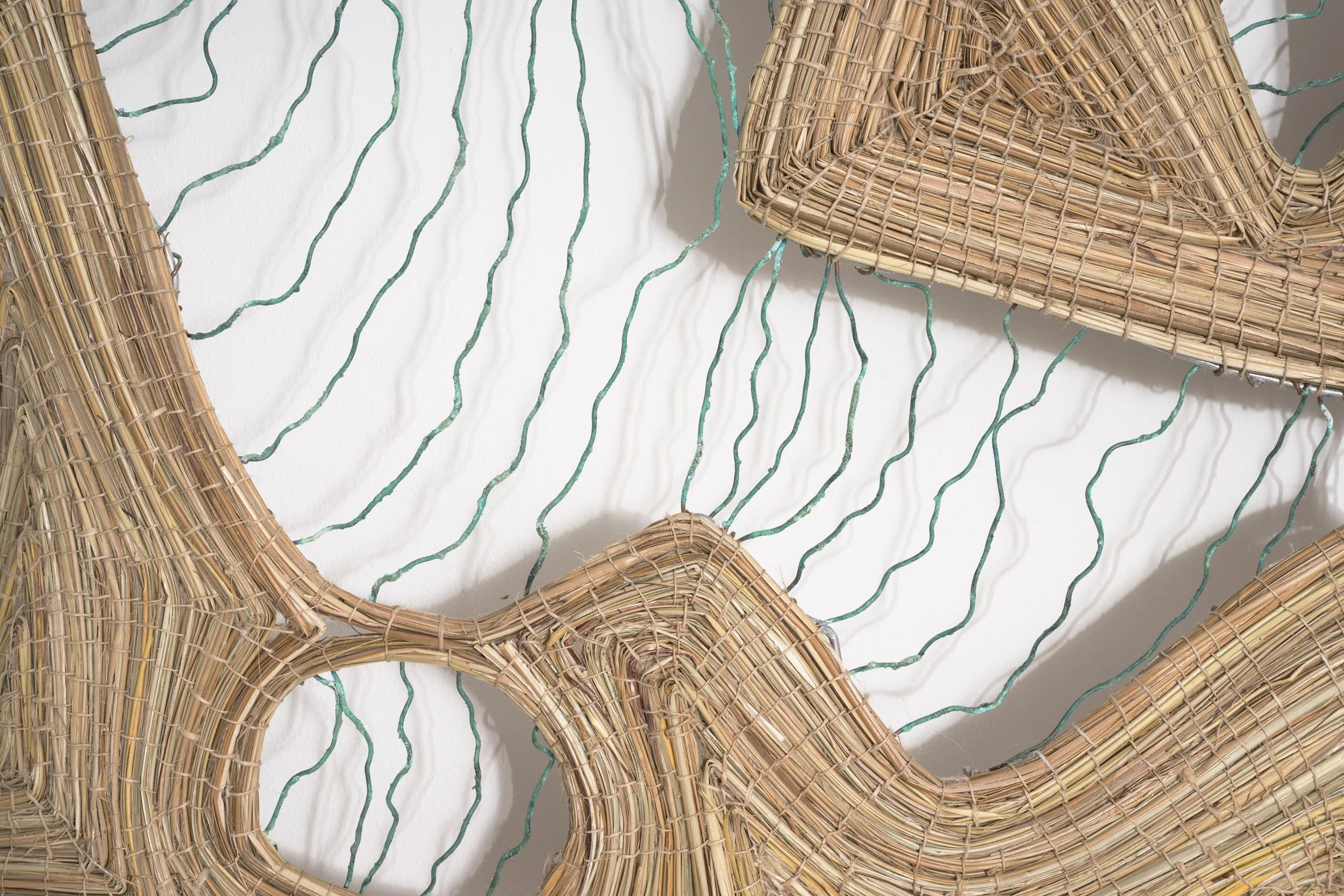 Woven straw baskets and green wire on a white wall.