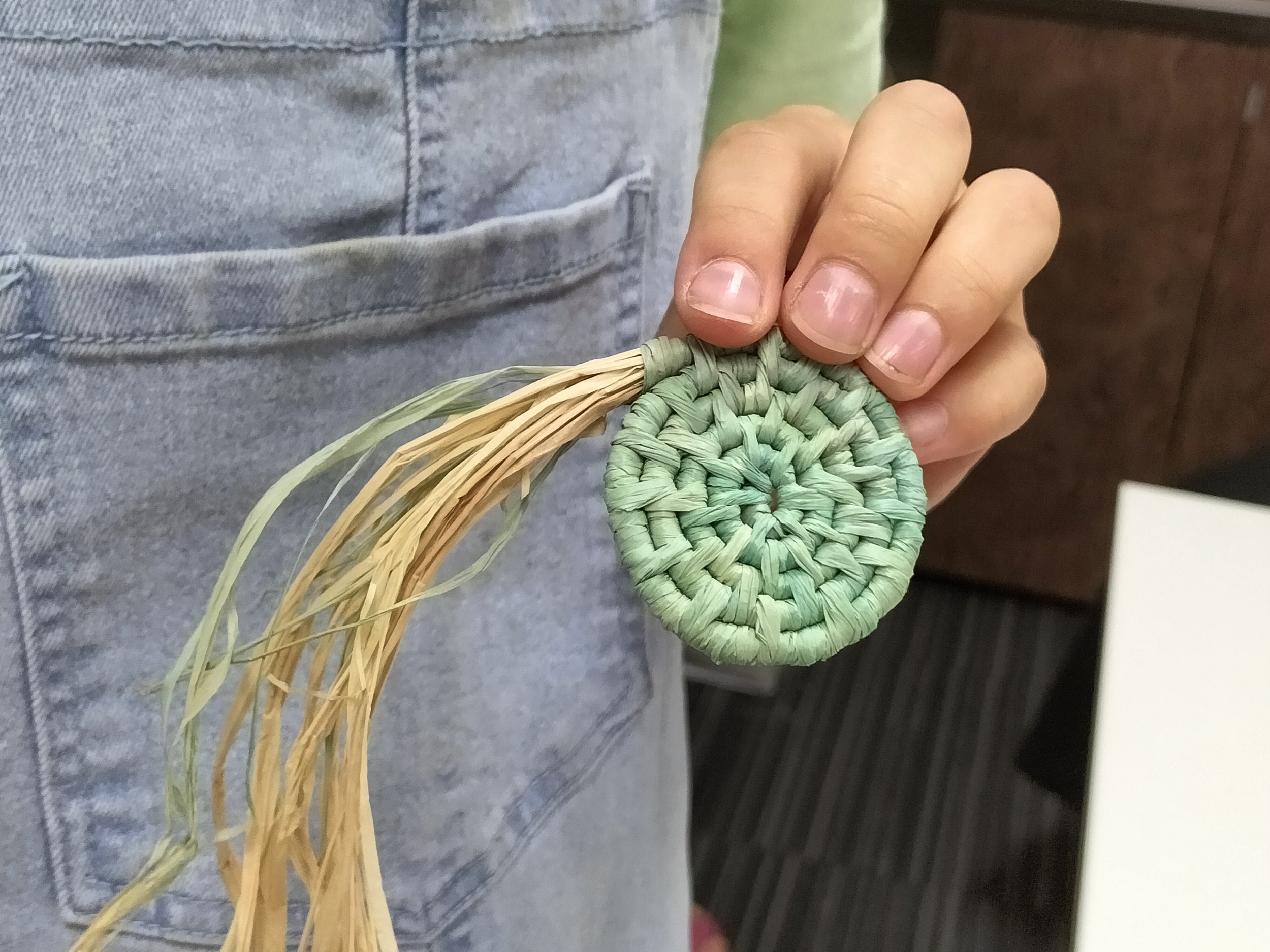 Close-up of a person holding the beginnings of a small coiled basket made of natural fibres, with the person's grey shirt visible.