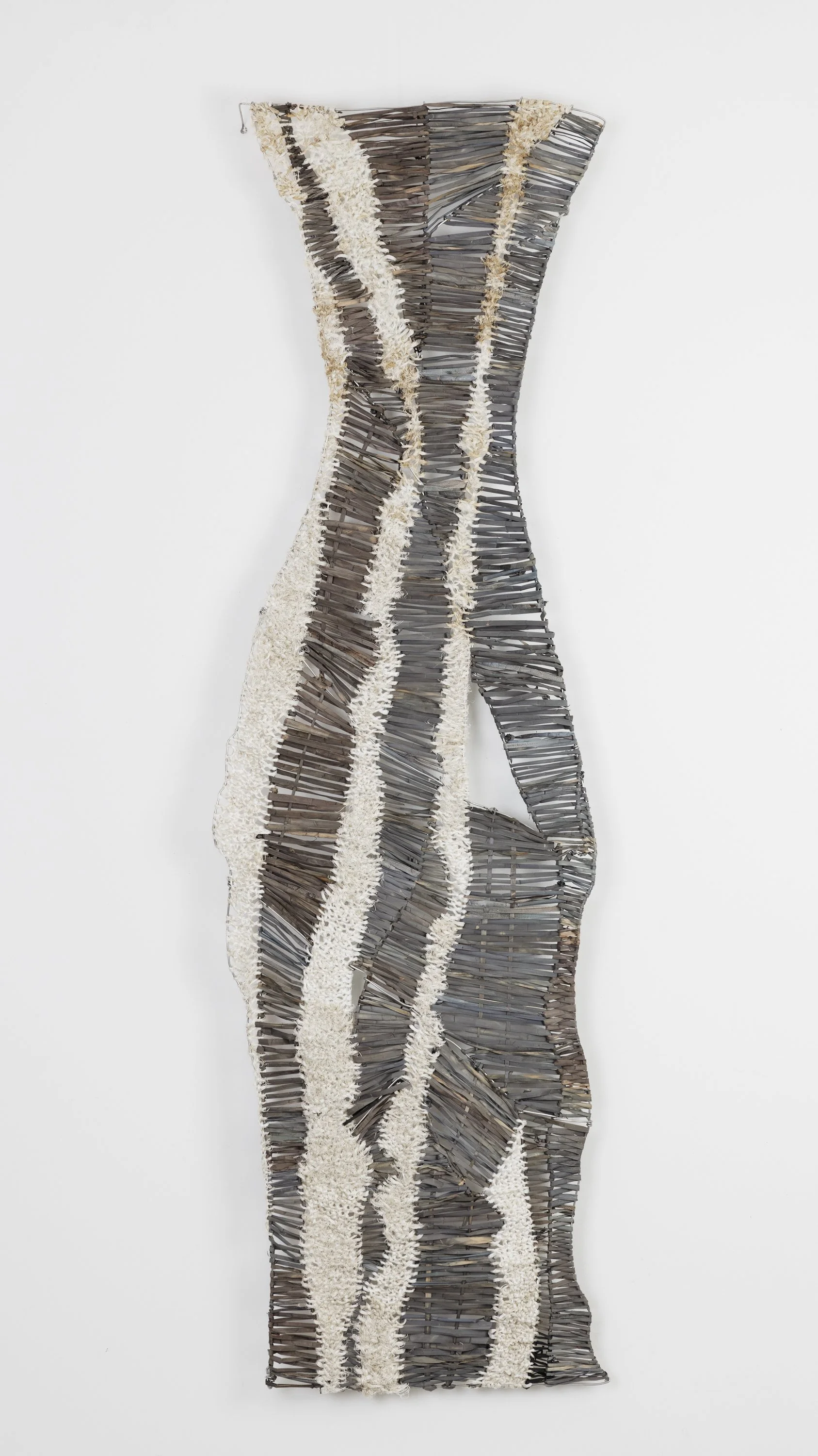 A woven art wall hanging featuring black, white, and beige wavy stripes.