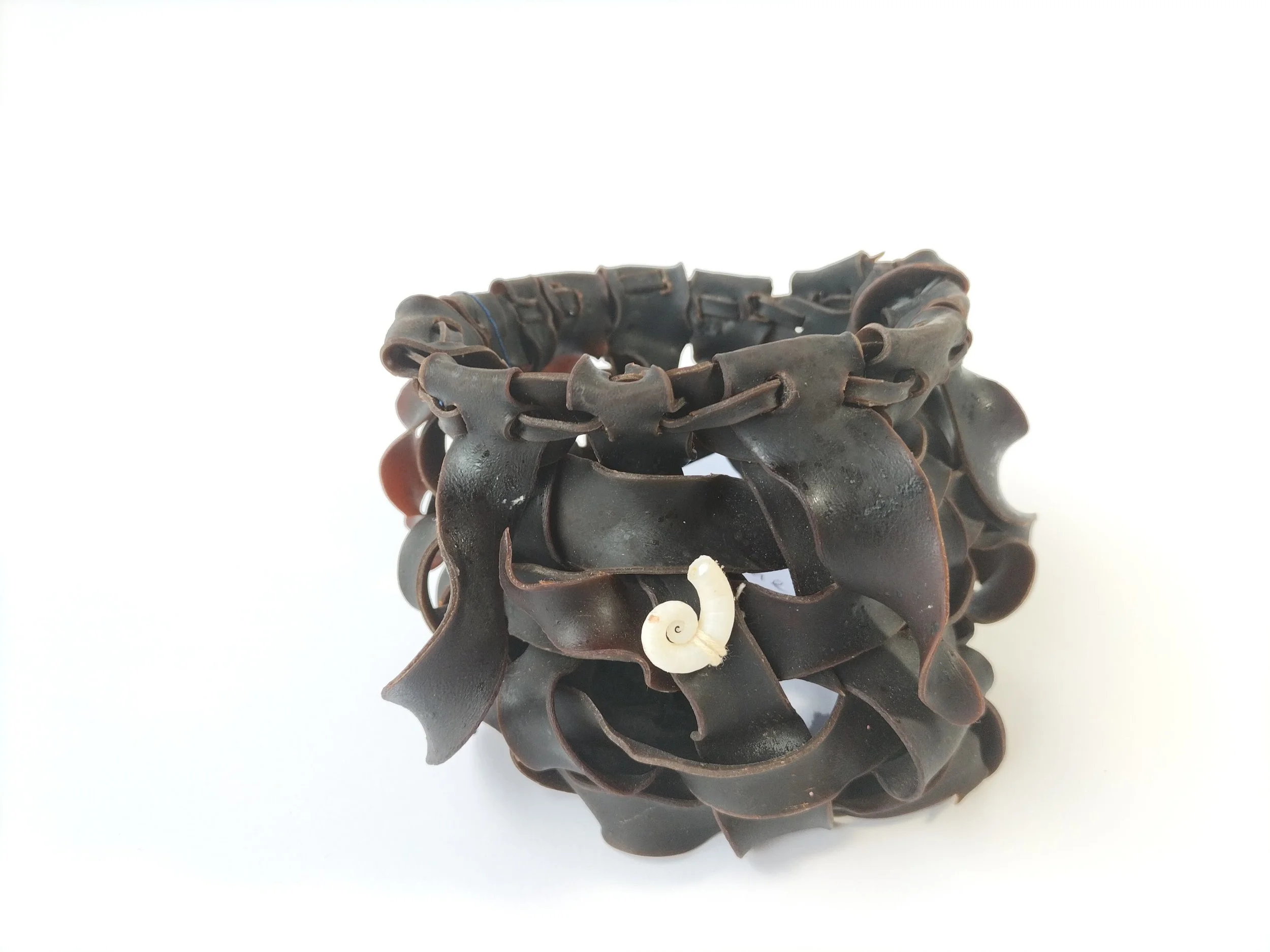 A brown rubber bracelet with an interconnected design, placed on a white surface.