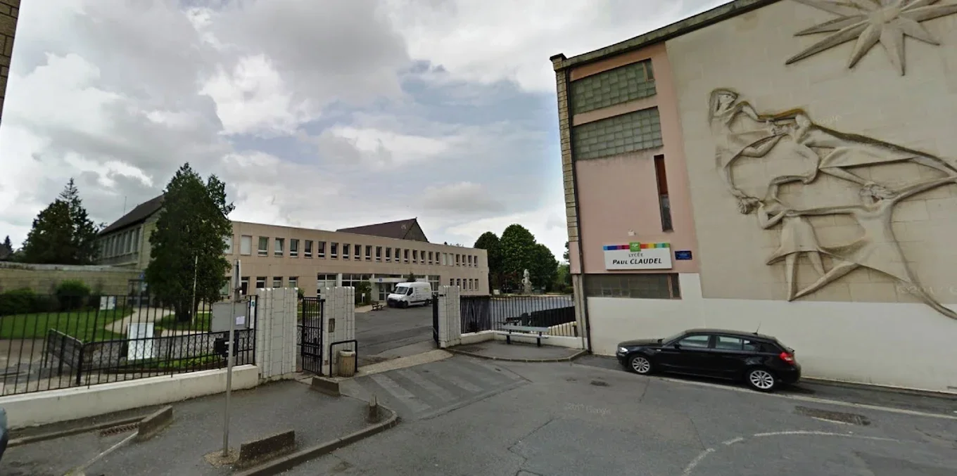 Vue d'une école avec un bâtiment principal et une sculpture en relief sur le mur côté droit, un panneau indiquant 'Lycée Paul Claudel', une voiture noire garée et un portail d'entrée.
