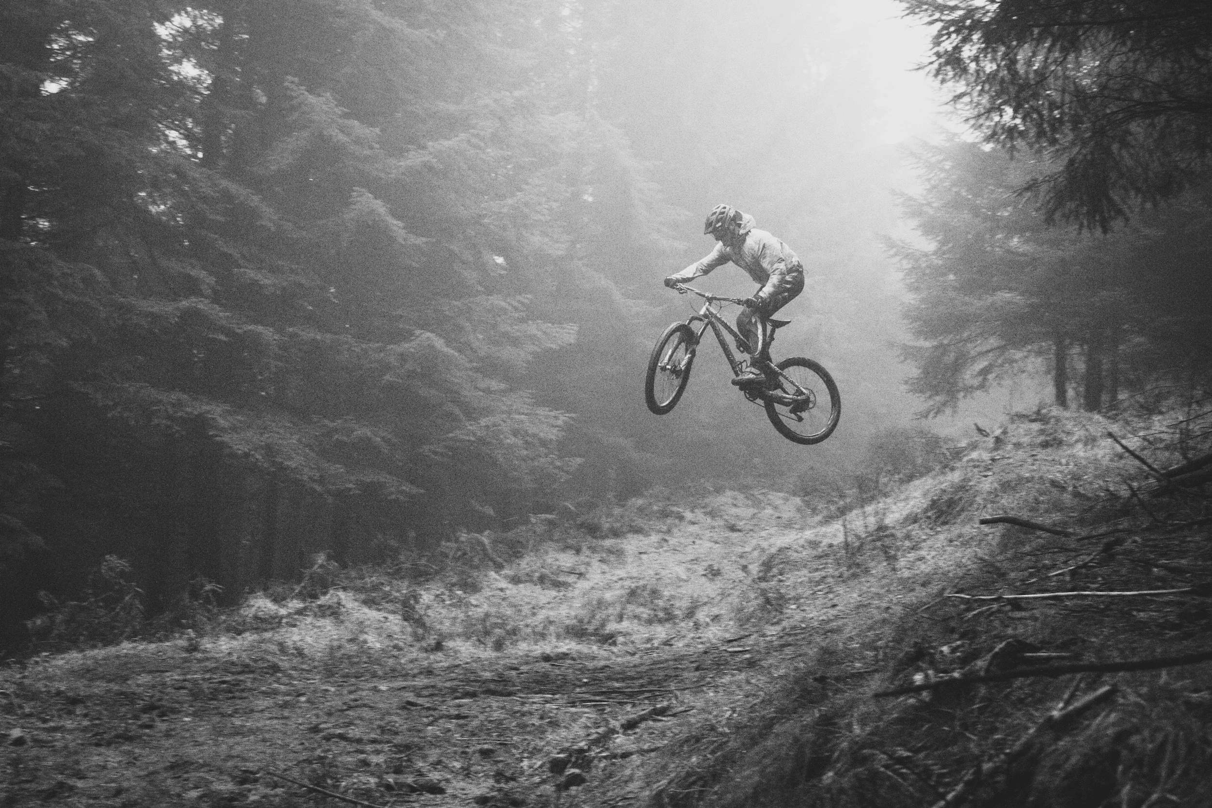 A person riding a mountain bike on a trail through a foggy forest.