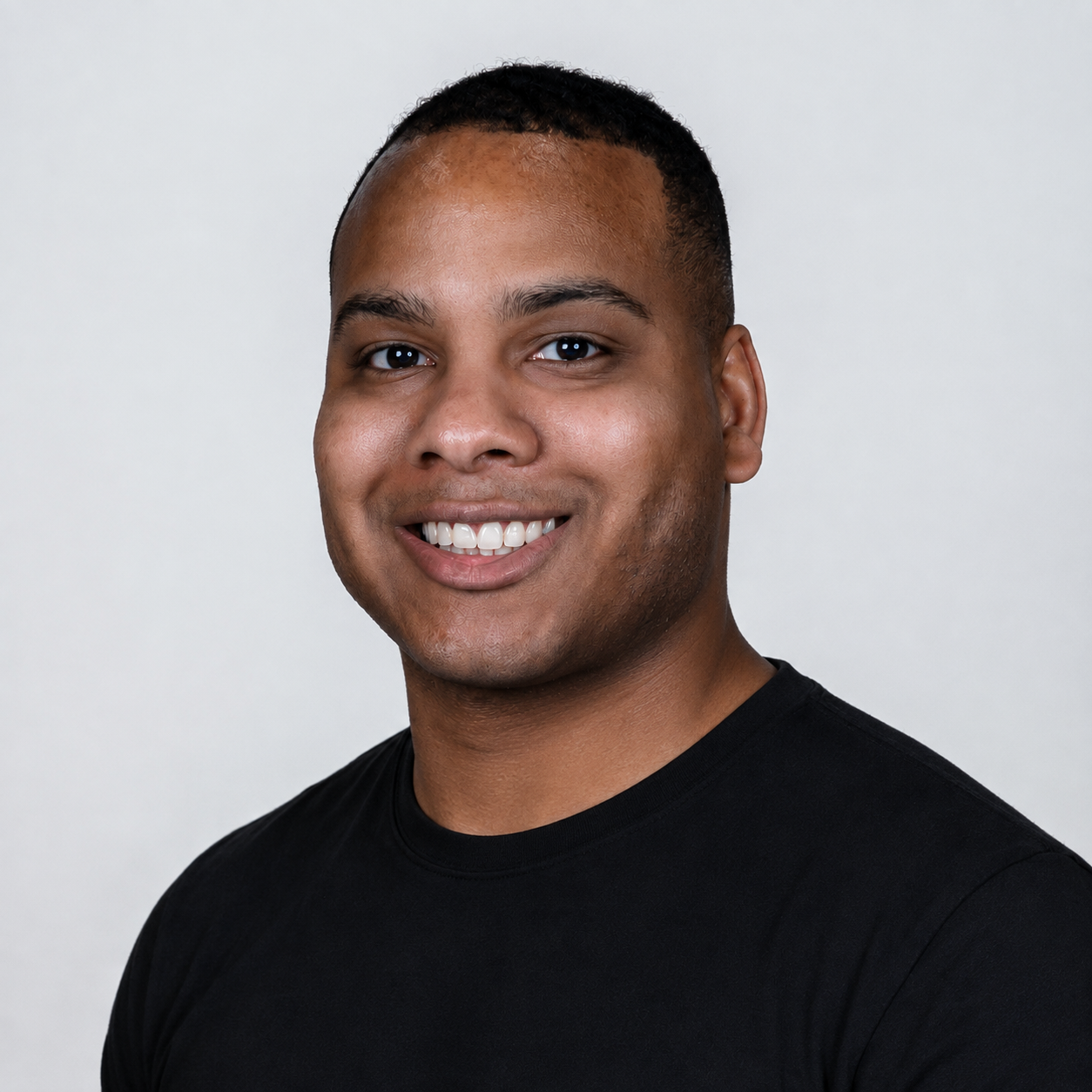 A smiling man with short black hair, dark eyes, and a black shirt against a plain gray background.