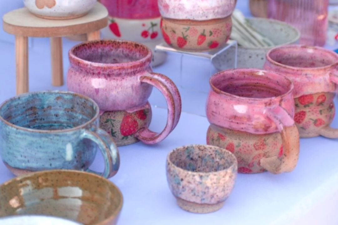 Colorful handmade ceramic mugs and cups with strawberry patterns on display.