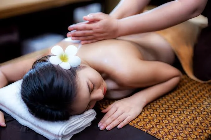 A woman receiving a massage while lying face down with a flower in her hair, on a massage table with a towel under her head and a patterned cloth.