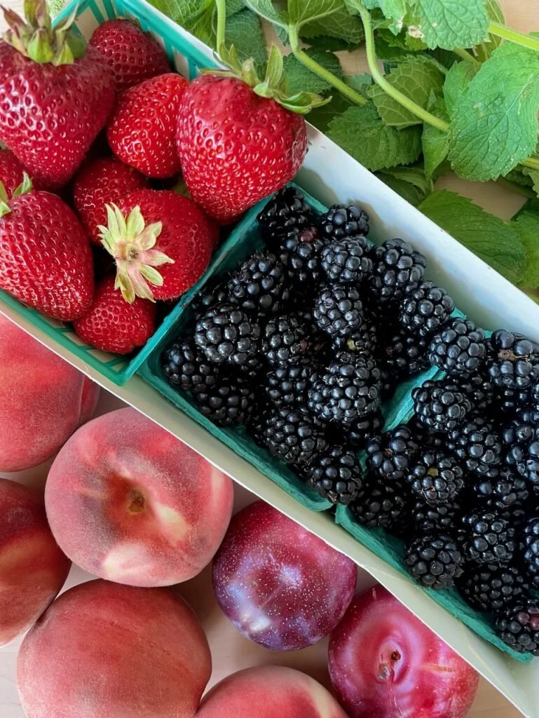 Fresh strawberries, blackberries, and peaches in a basket.