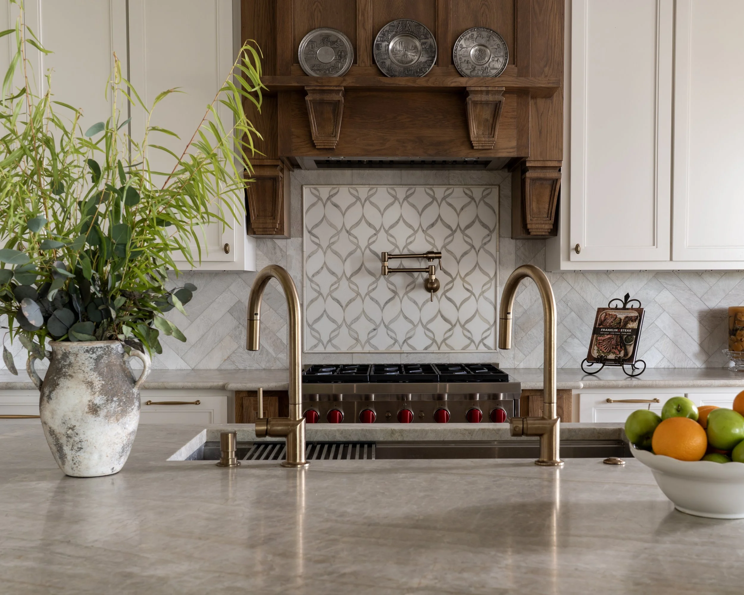 Modern kitchen with center island, potted plant, and decorative plates on wooden vent hood.