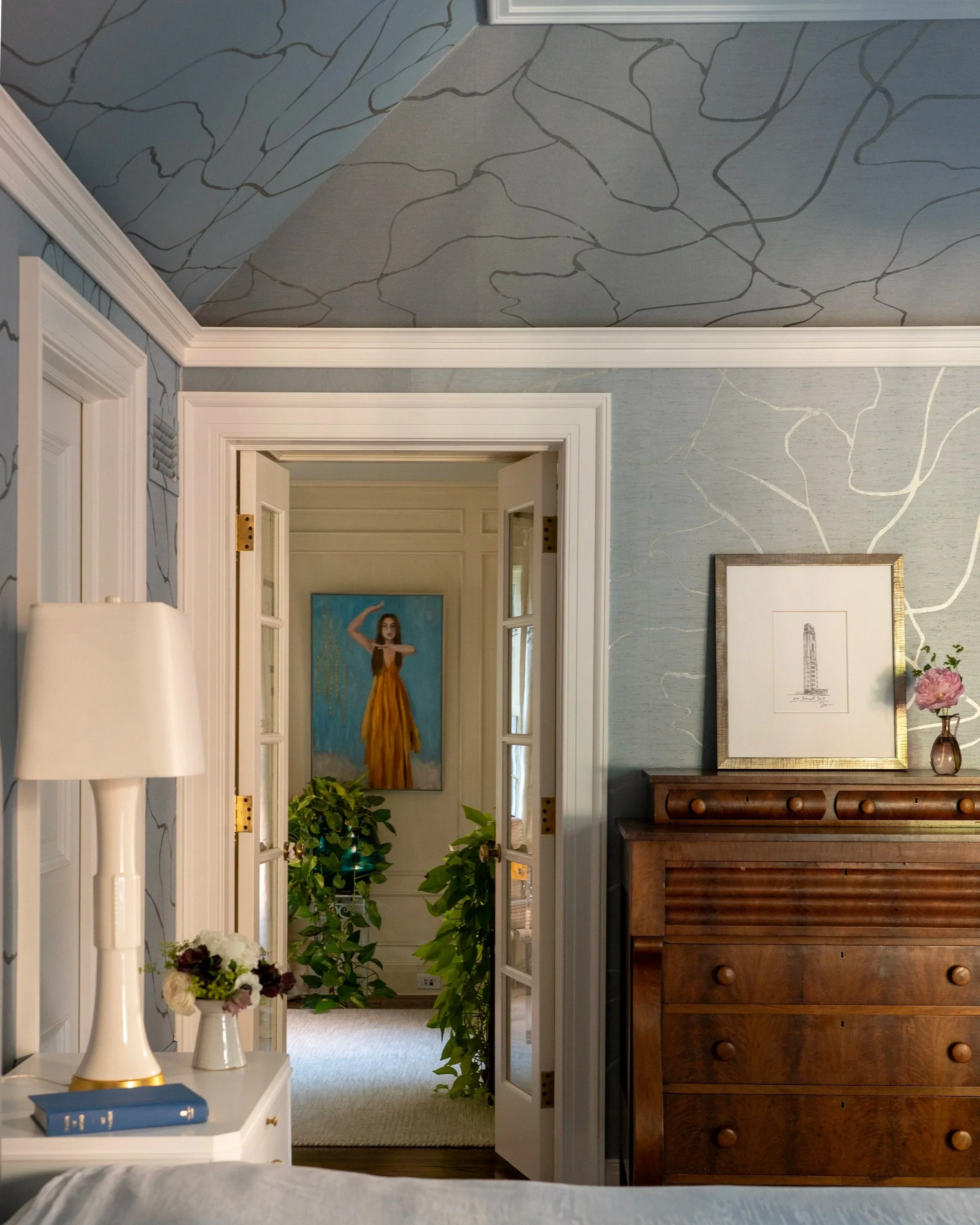 Wallpapered room with an antique wooden dresser looking into a room with a painting of a girl taken in Chicago, IL.