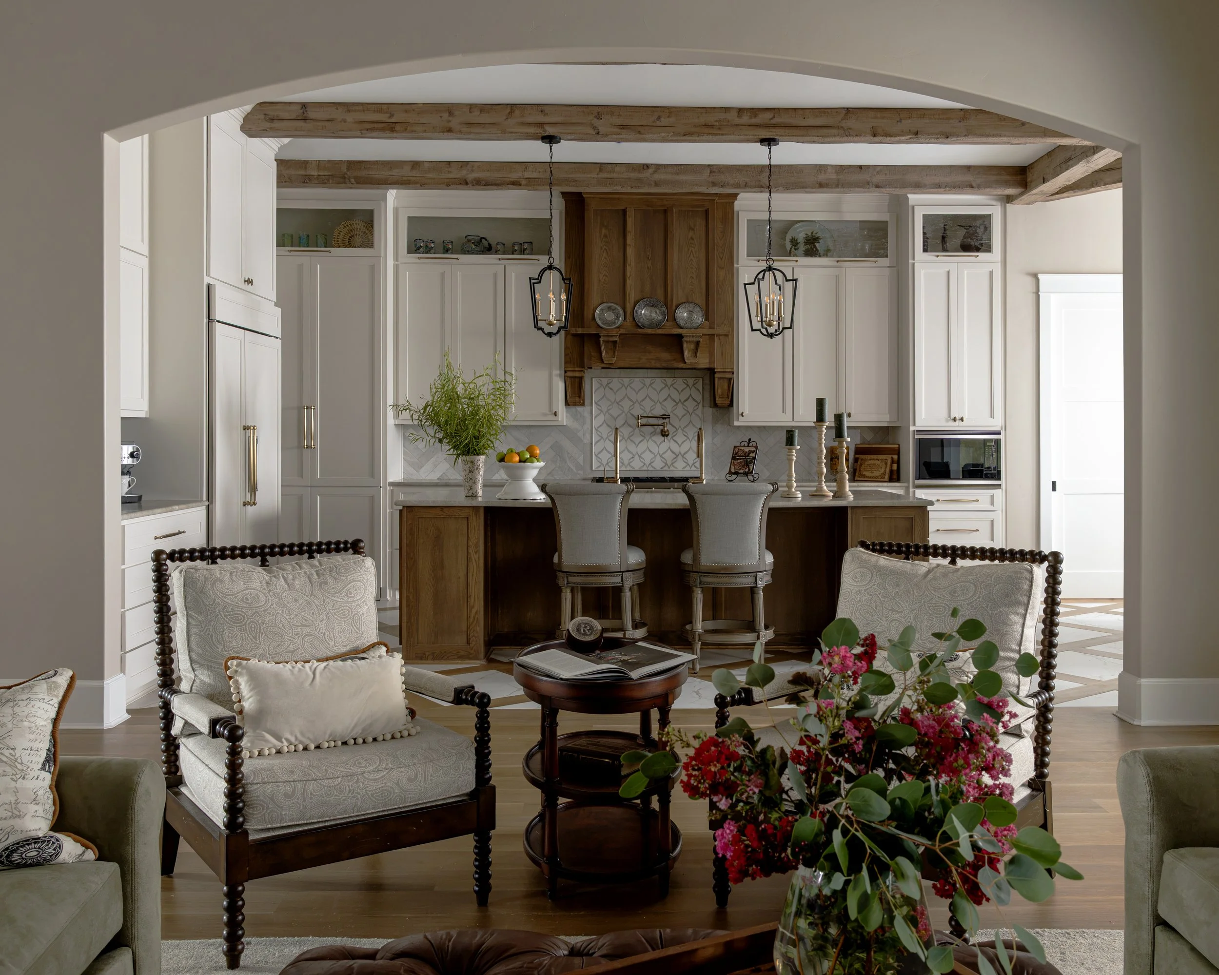 Living room with white and wooden cabinetry, hanging pendant lights, and a table with a bowl of fruit. A floral arrangement is in the foreground.