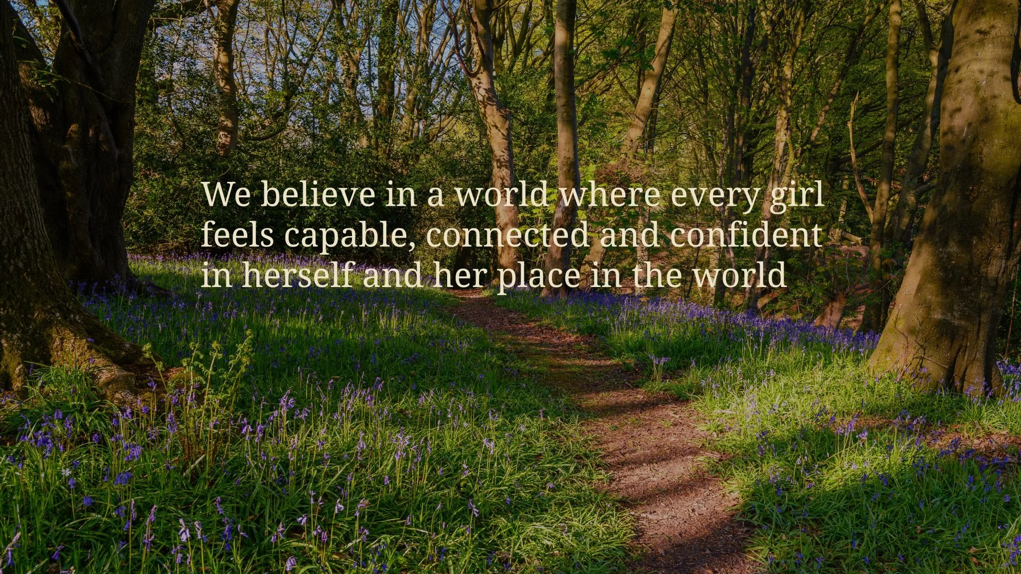 A forest pathway with green trees and purple flowers, with an inspirational quote about believing in girls.