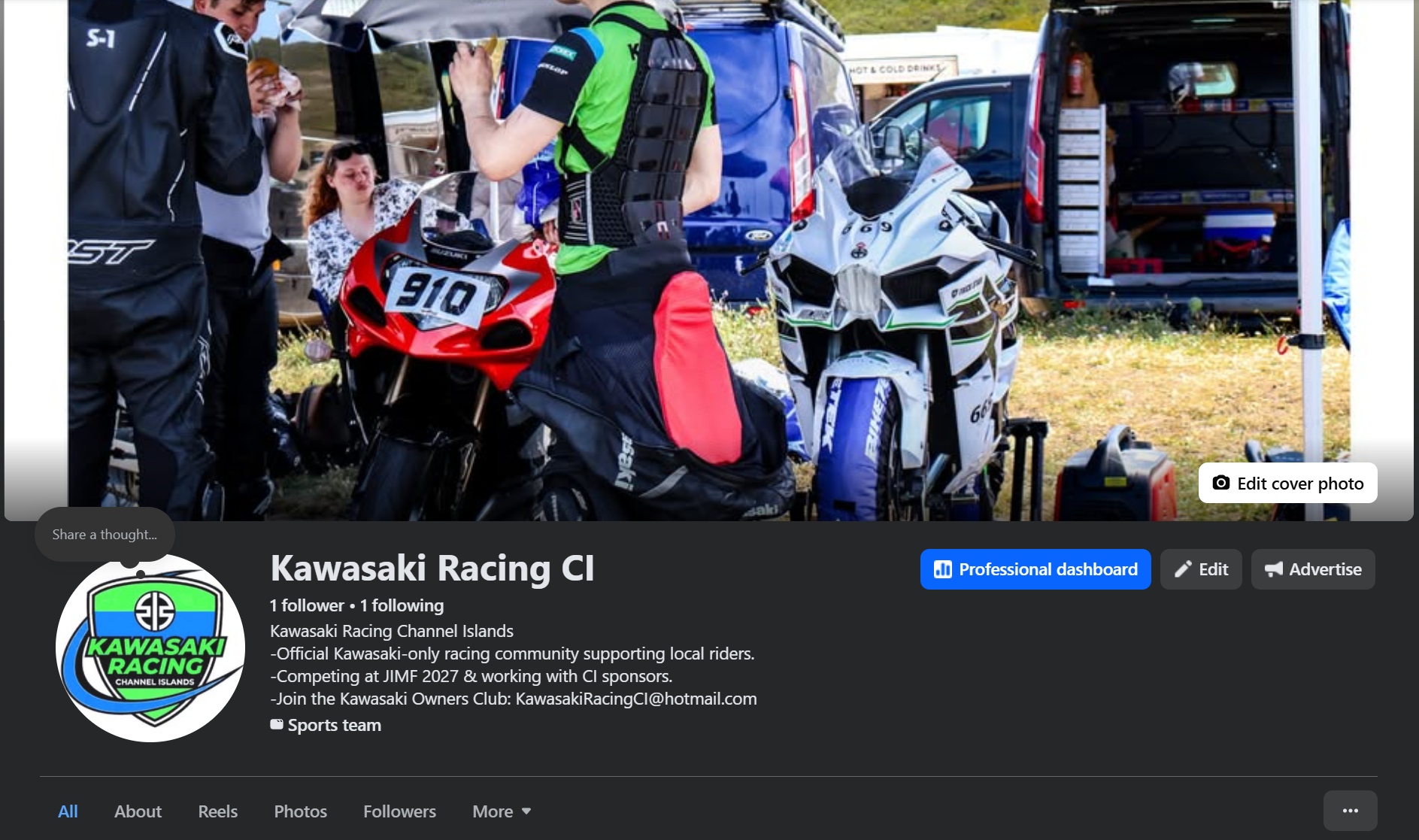 At a Kawasaki Racing Club community event, several people are gathered around two race motorcycles, one red with the number 910 and a green, black, and white one. There are tents and a vehicle in the background, and the scene is outdoors on a grassy area.
