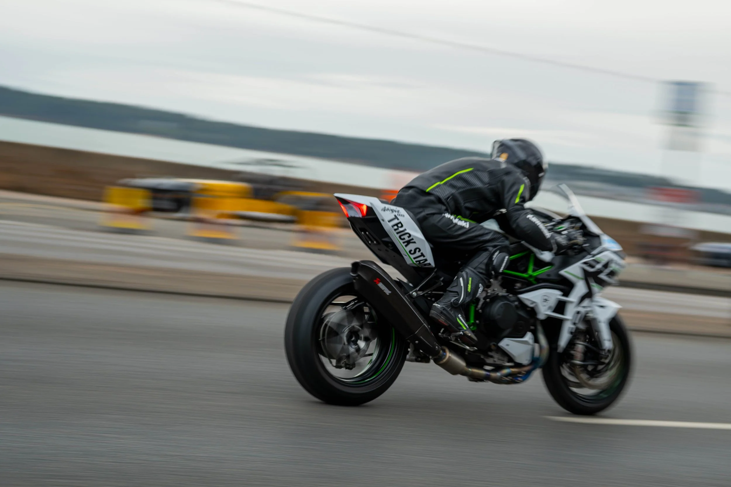 A motorcyclist wearing black gear and a helmet riding a sportbike at high speed on a racetrack, with a blurred background indicating motion.
