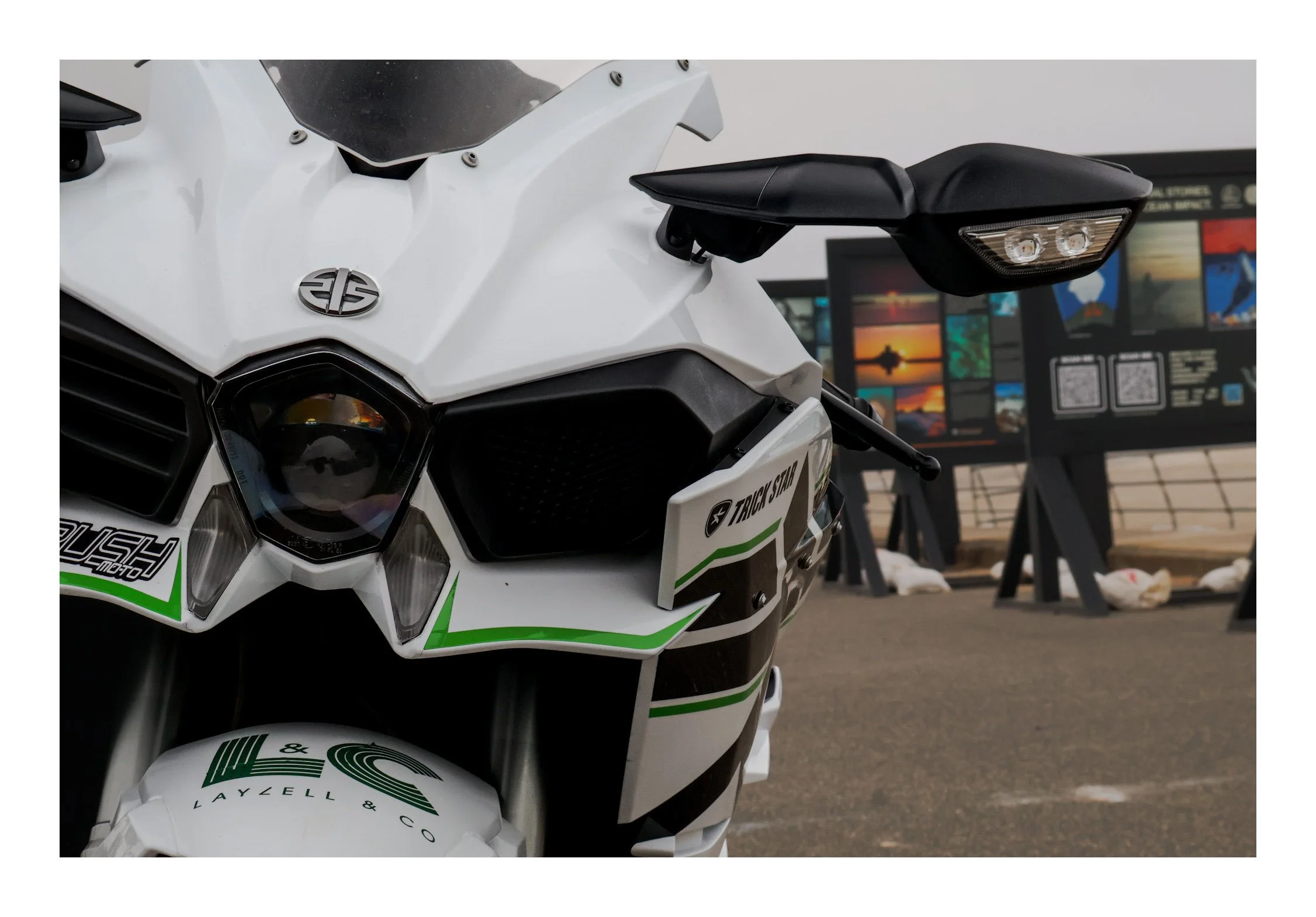 Close-up of a white and black motorcycle with green accents, parked indoors with a colorful display in the background.