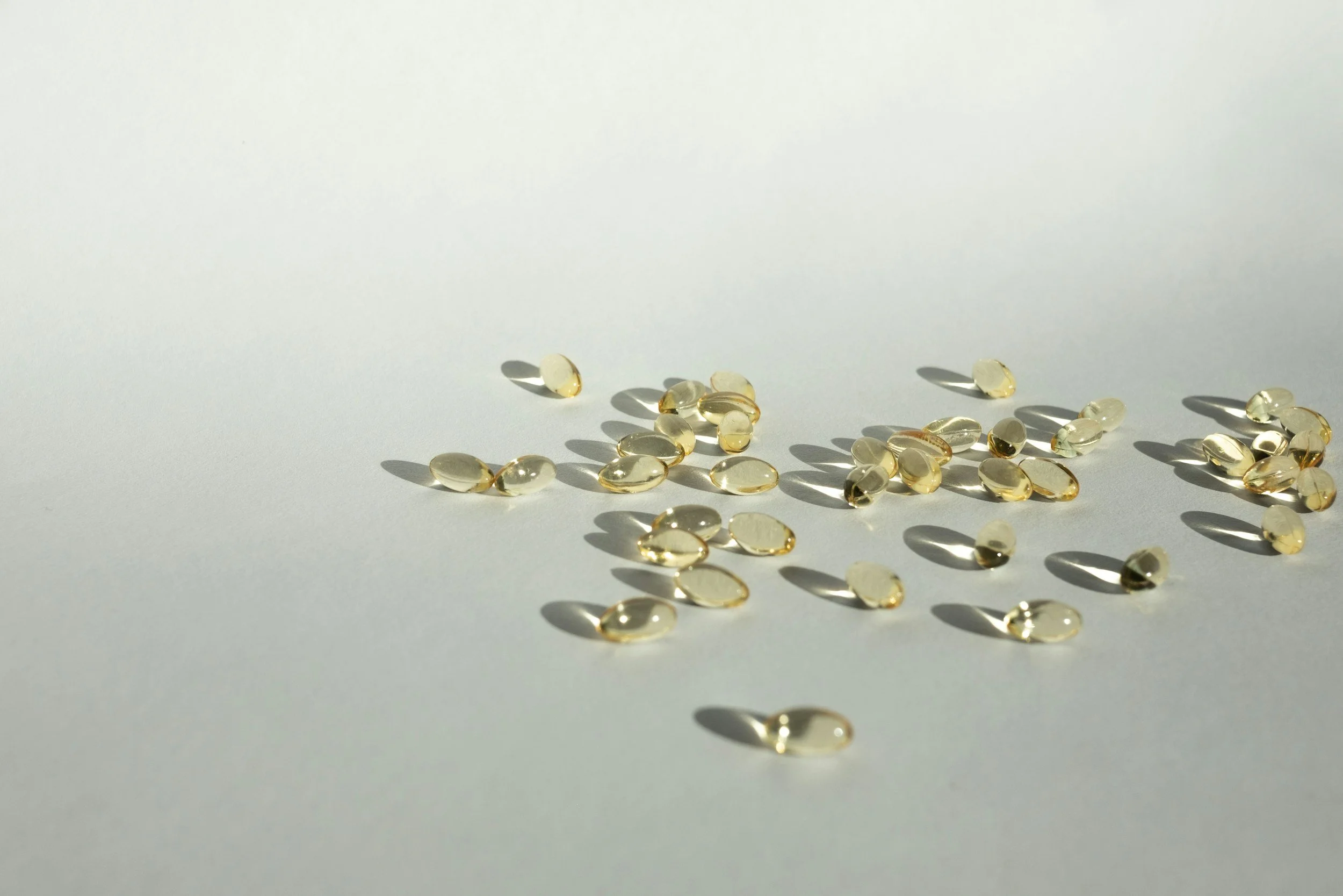Small translucent capsules with a yellowish tint scattered on a white surface, casting shadows.