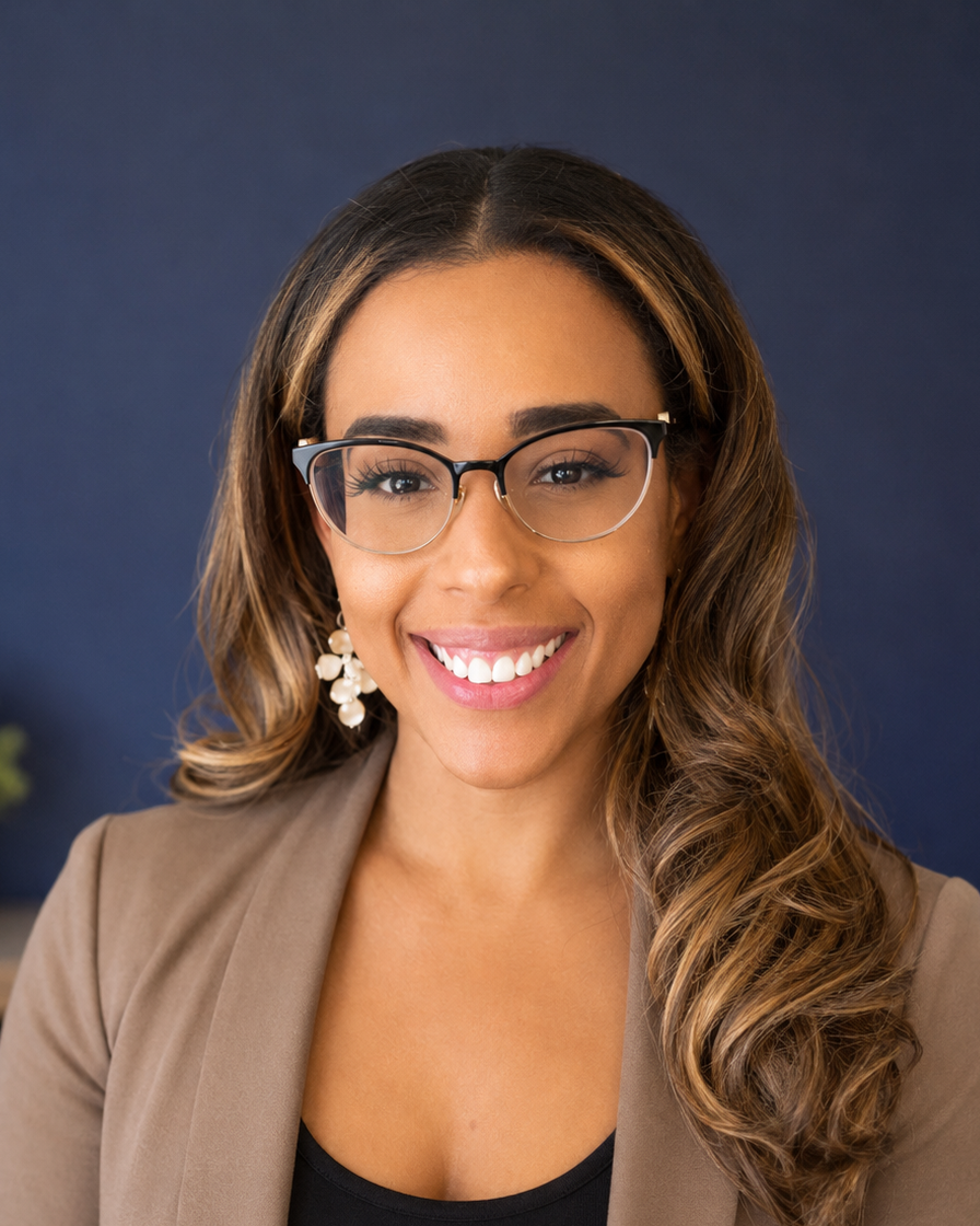 A smiling woman with wavy brown hair, glasses, and earrings, wearing a taupe blazer and black top, against a dark background.