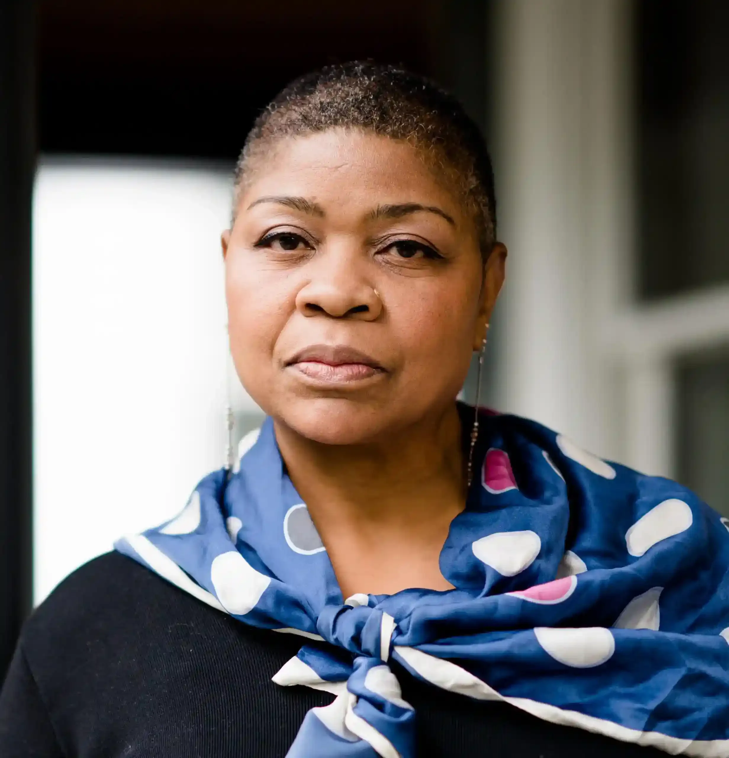 Black woman with short haircut and blue patterned scarf over black top