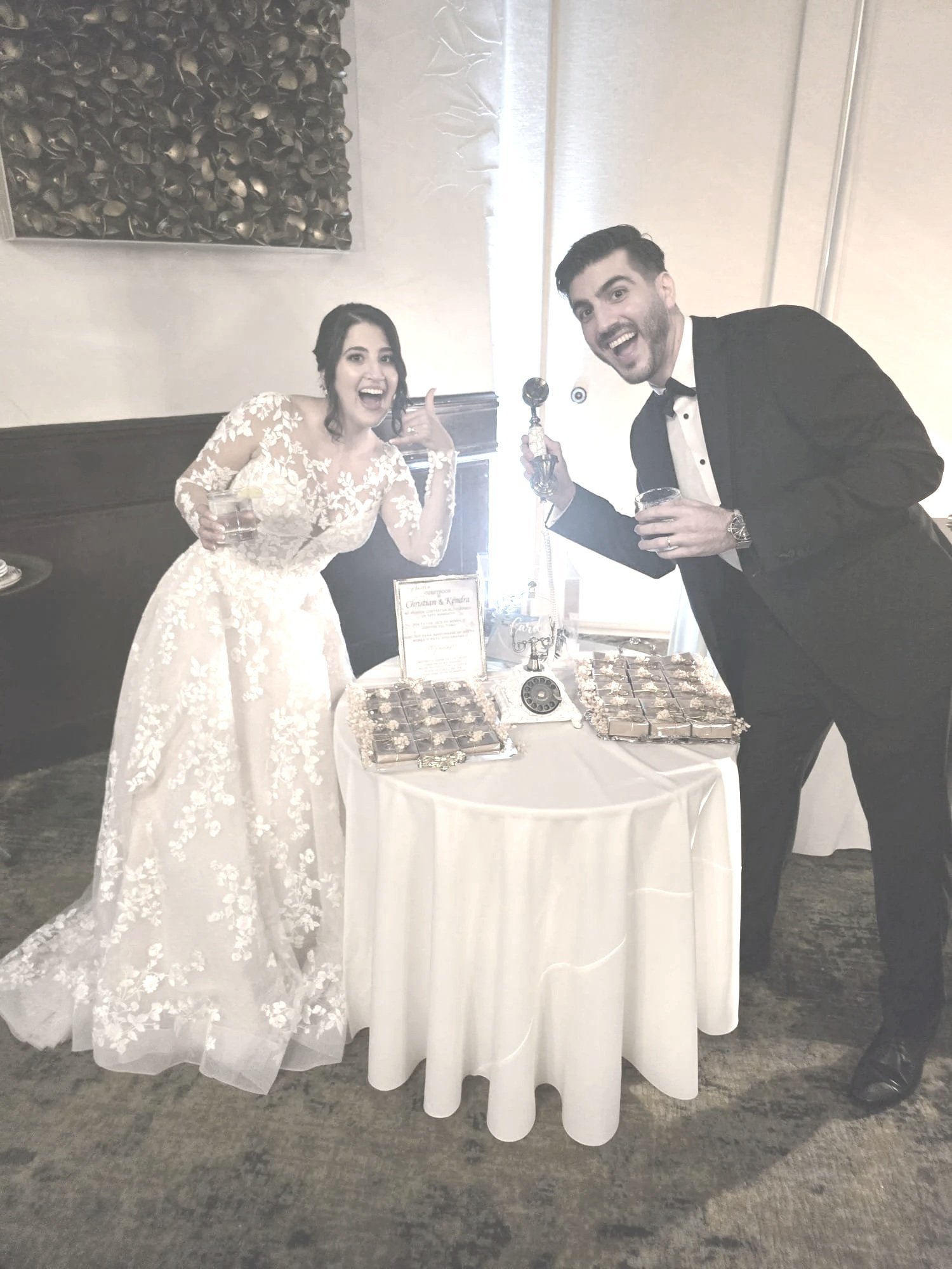 Excited bride and groom posing at their wedding reception table while recording a voice message on a vintage Memories Out Loud audio guestbook phone.
