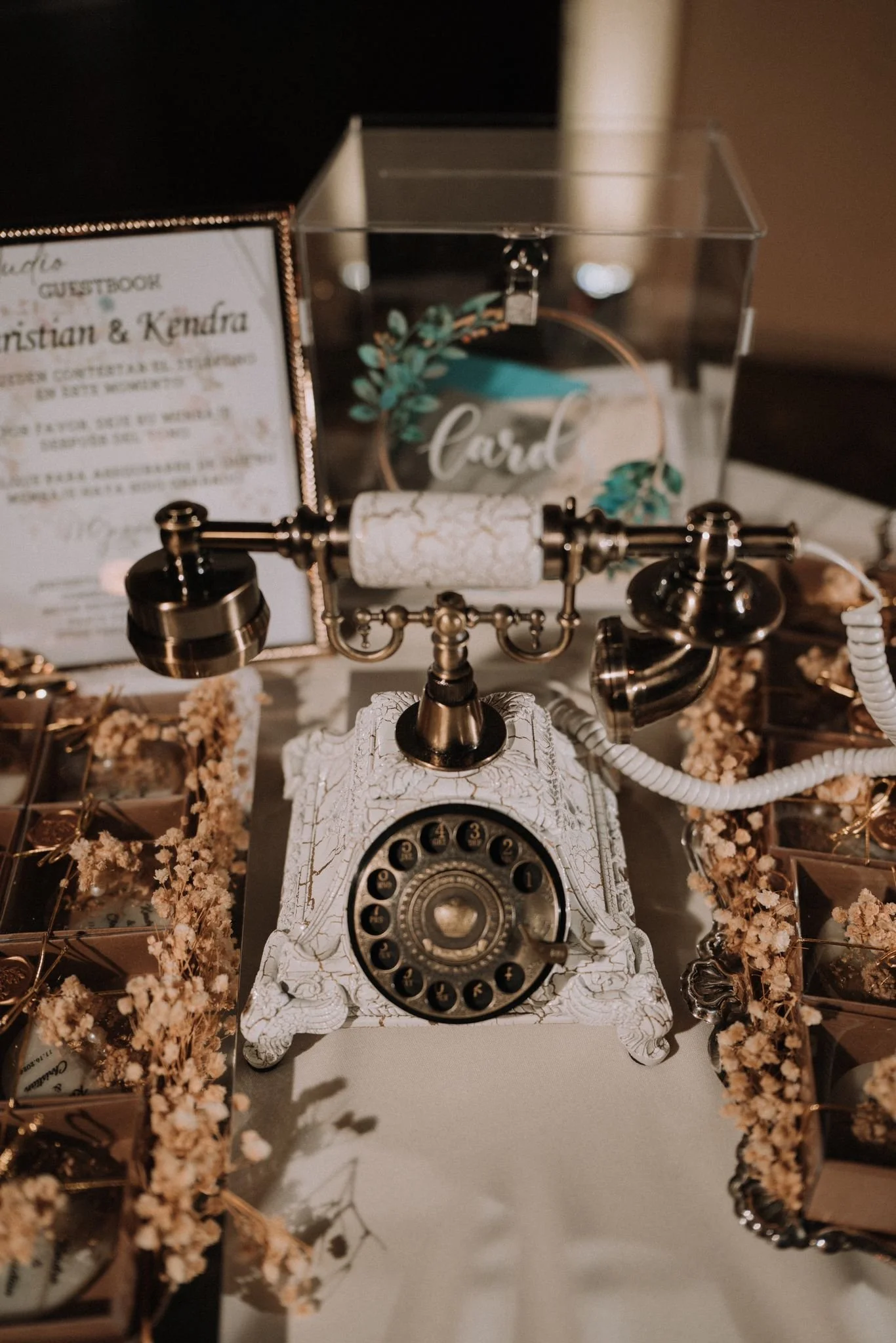Ornate white and brass vintage audio guestbook phone displayed on a wedding reception table surrounded by dried floral favors and an acrylic card box.