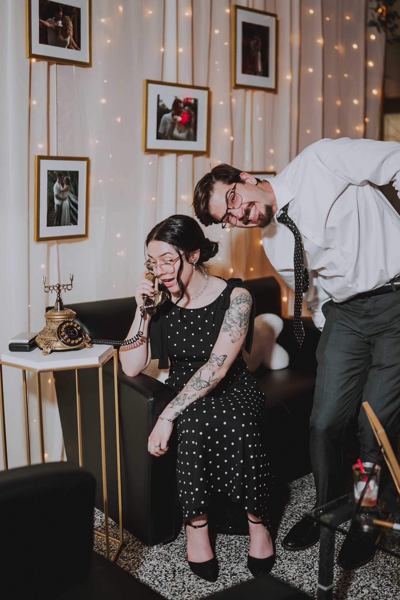 Wedding reception guests having fun while recording a message on an antique brass audio guestbook phone in a lounge area with fairy lights.