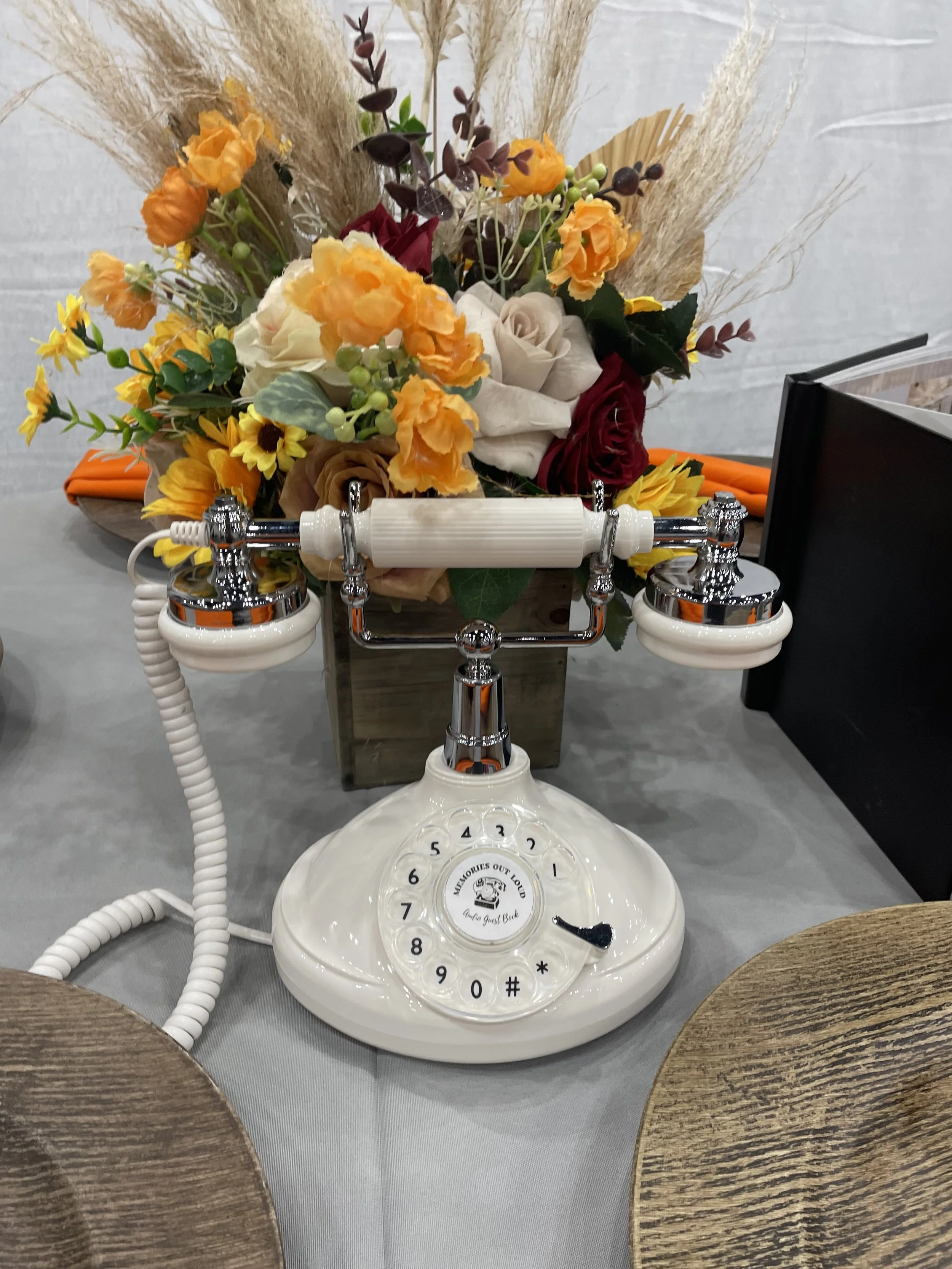 A cream and chrome Memories Out Loud vintage audio guestbook phone featured in front of a warm orange and yellow floral centerpiece at an event.