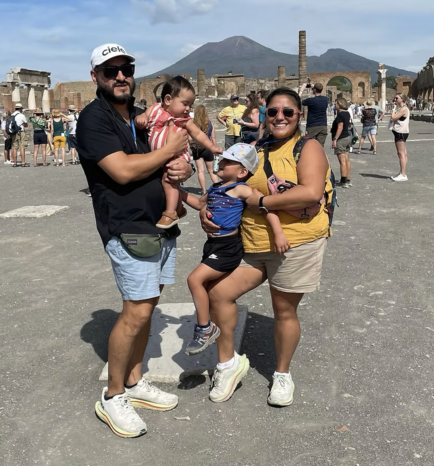 John and Debbie, owners of Memories Out Loud, posing on a family vacation with their two young children at the ancient ruins of Pompeii with Mount Vesuvius in the background.