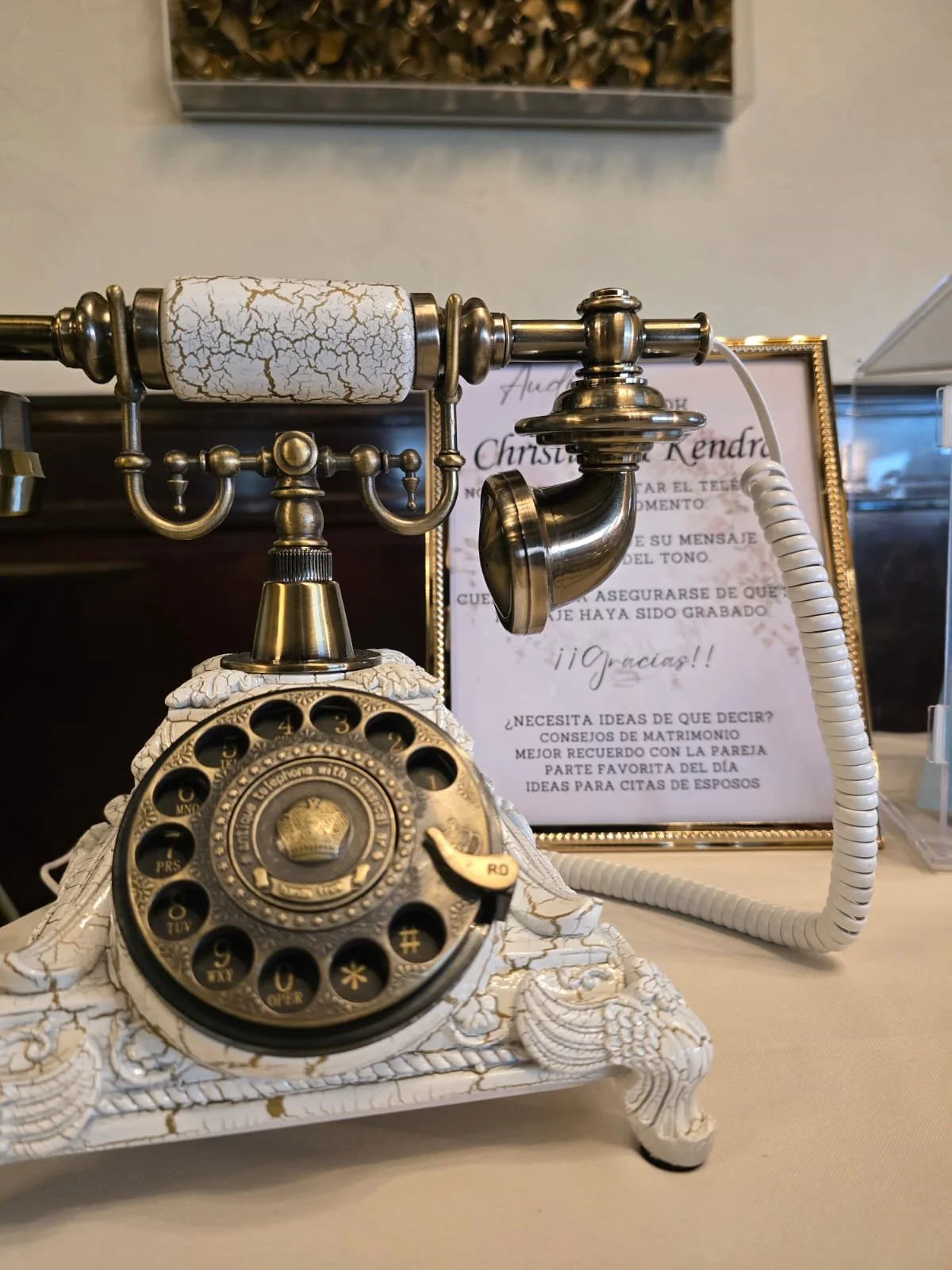 Close-up of the Charlotte vintage ornate brass and white audio guestbook phone with framed Spanish instructions at a wedding reception.