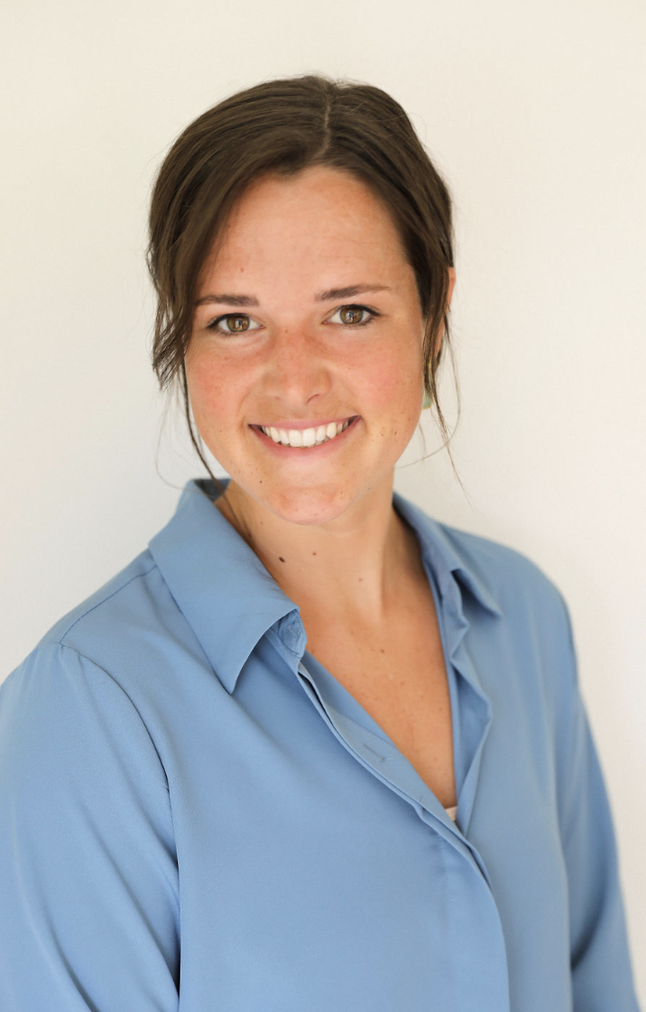 Close-up of a smiling young woman with brown hair wearing a light blue collared shirt.