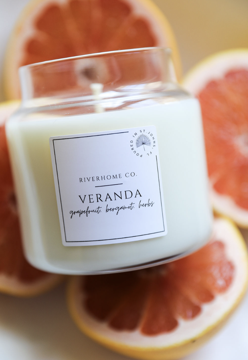 A white candle labeled 'Veranda' with grapefruit, bergamot, and herbs, surrounded by sliced grapefruits.