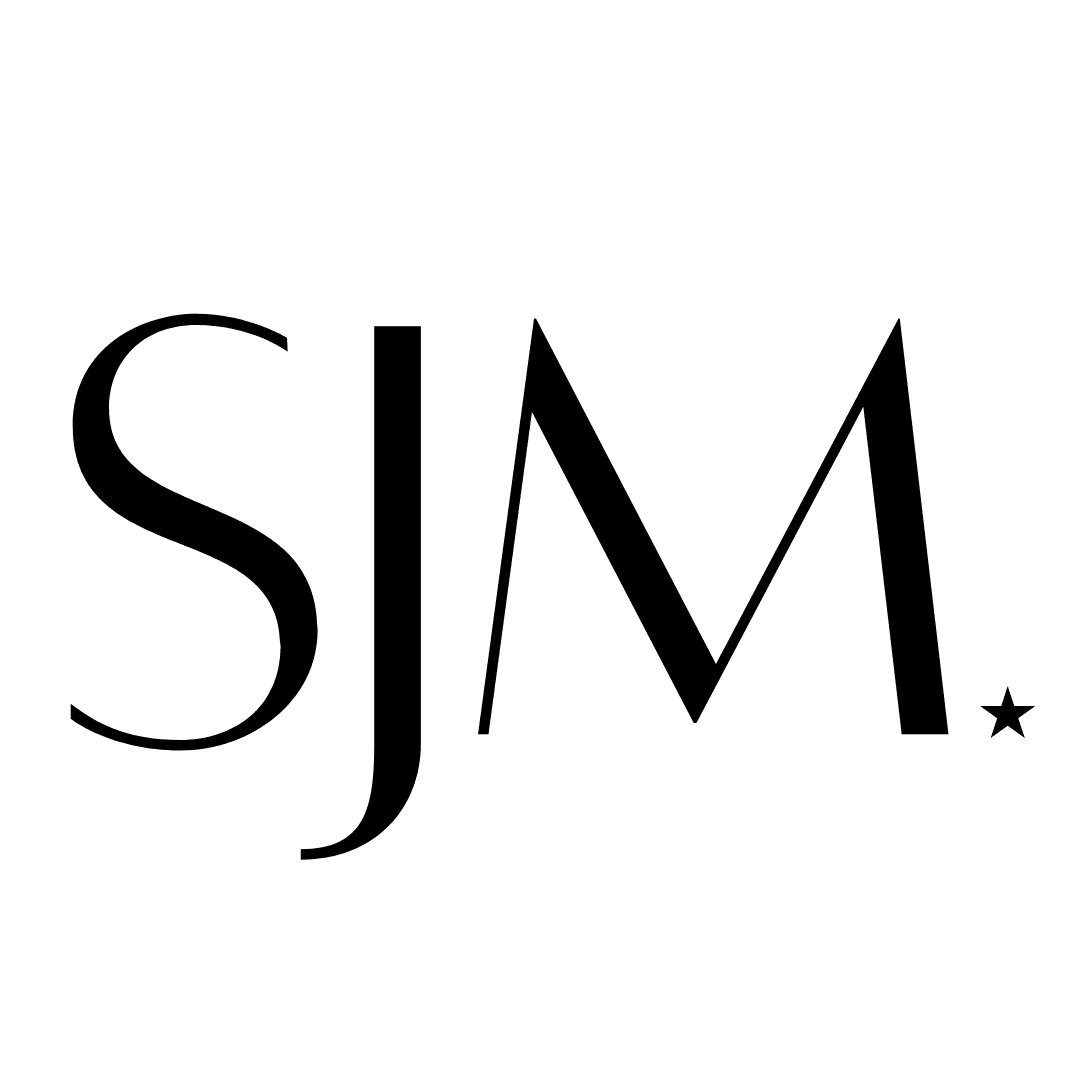 Silhouette of a person with a ponytail doing a handstand on one hand on a beach at sunset, with a wooden pier and sailboats in the background.