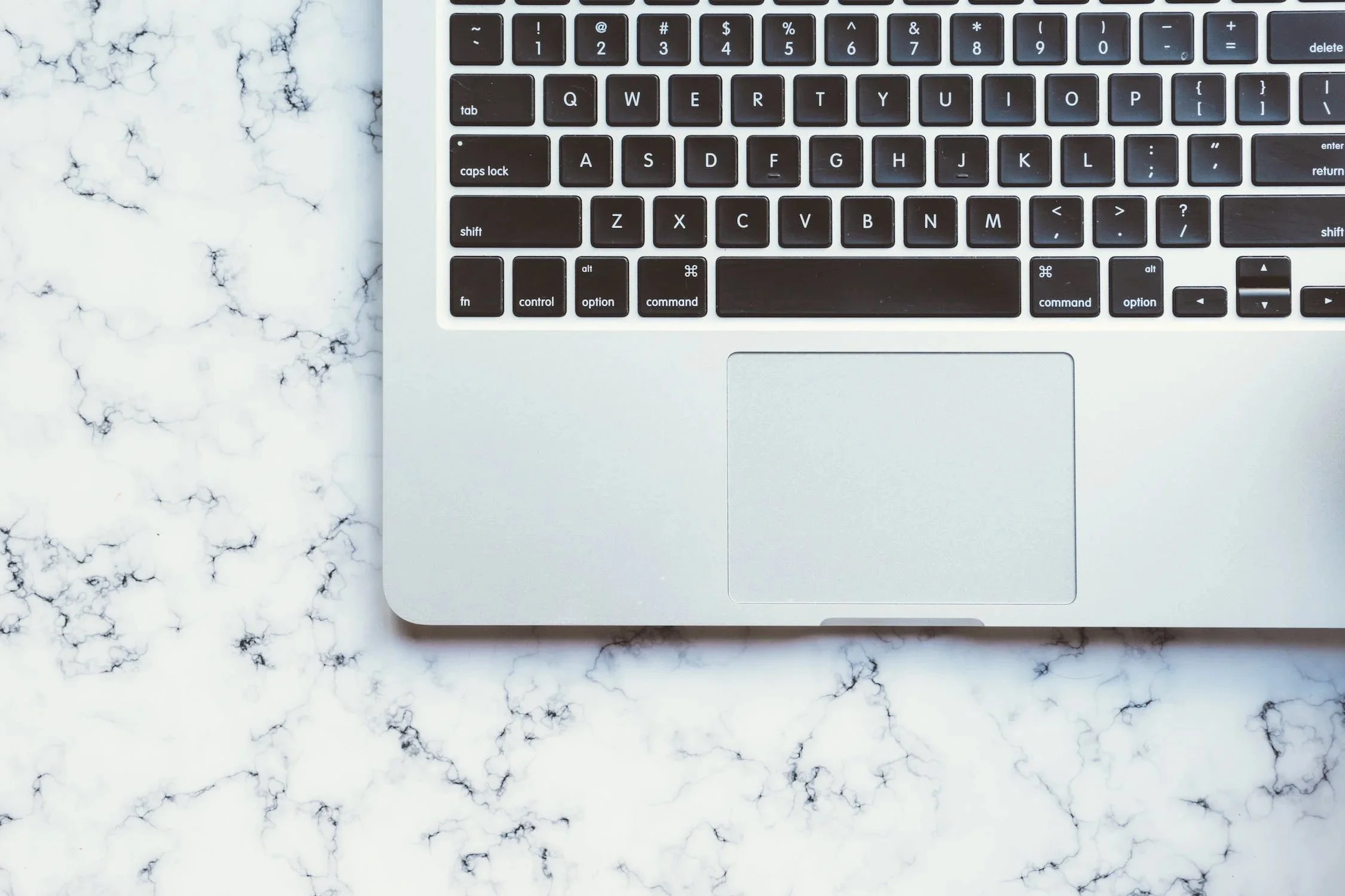 Top right corner of a silver laptop keyboard on a white marble surface.