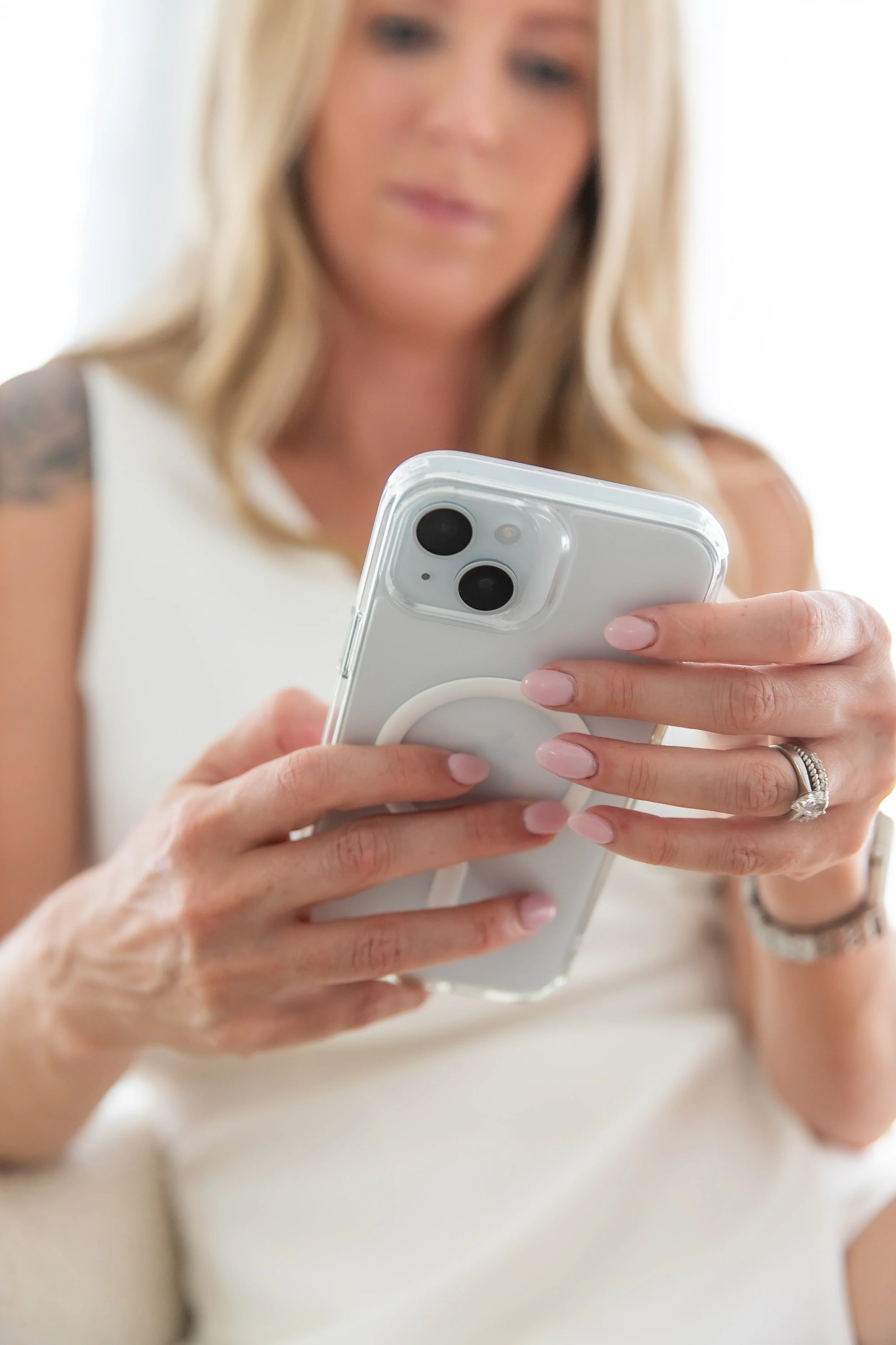A woman with blonde hair and a ring on her left hand uses a white smartphone with a pop socket.