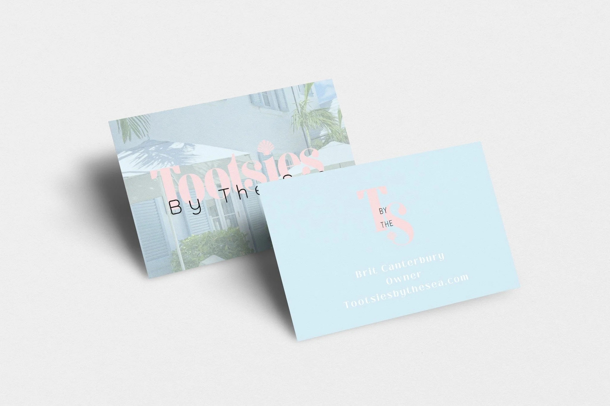 Business cards for Tootsie by the Sea, owned by Brit Canterbury, with a pastel blue and pink color scheme. One card displays a photo of a house with patio umbrellas and green foliage and the other shows contact information.