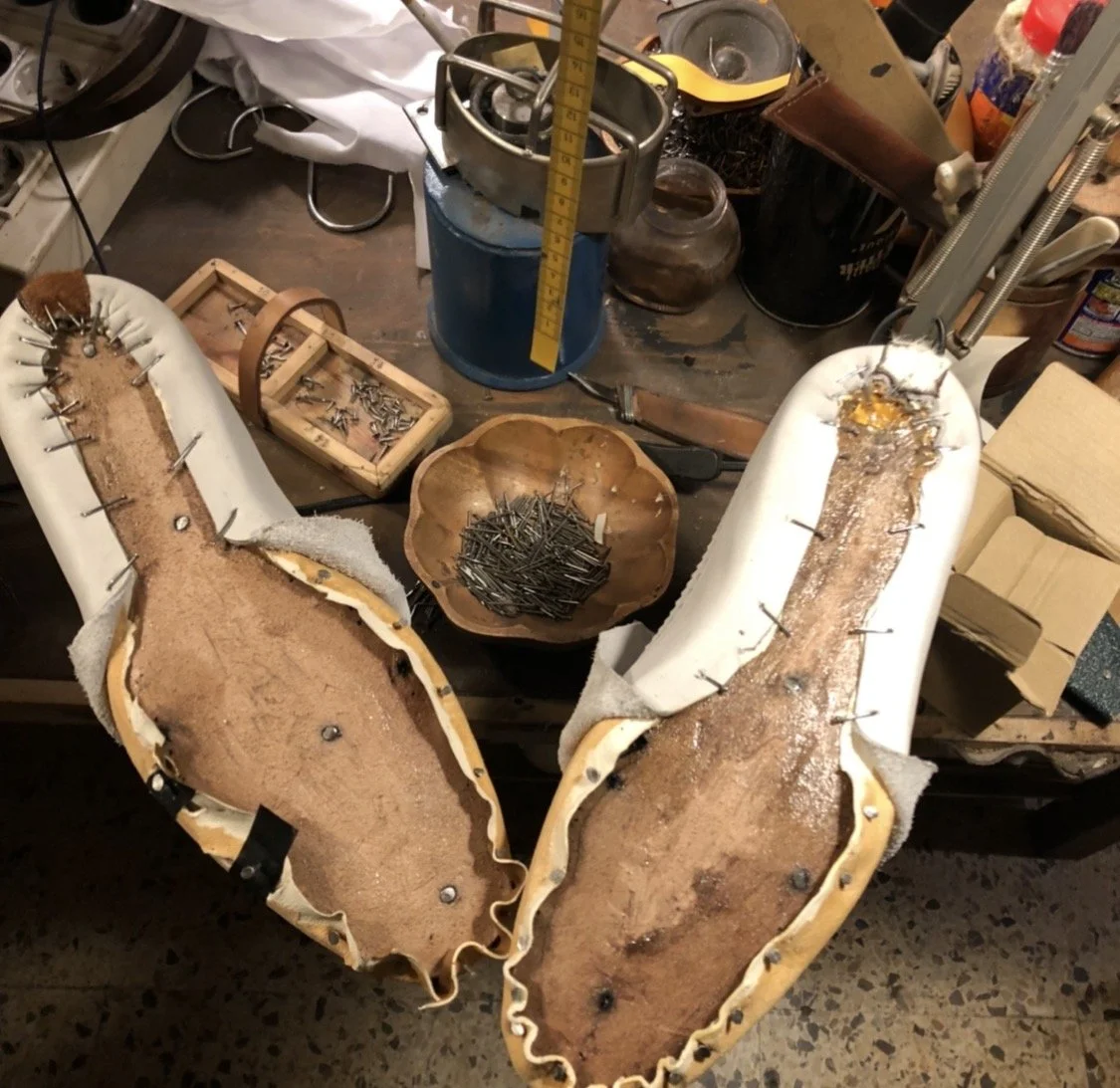 Proceso de reparación de una bota o zapato con tachuelas, incluyendo plantillas y herramientas en una mesa de trabajo.