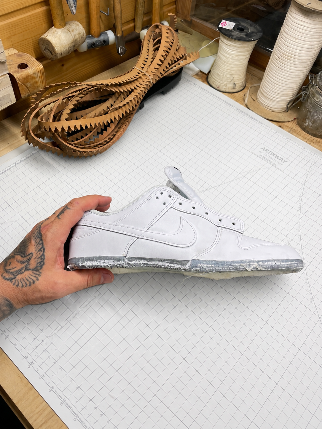 Zapato de baloncesto Nike hecho de material que parece papel o cartón, colocado sobre una tabla de dibujo con cuadrícula en un taller de artesanías