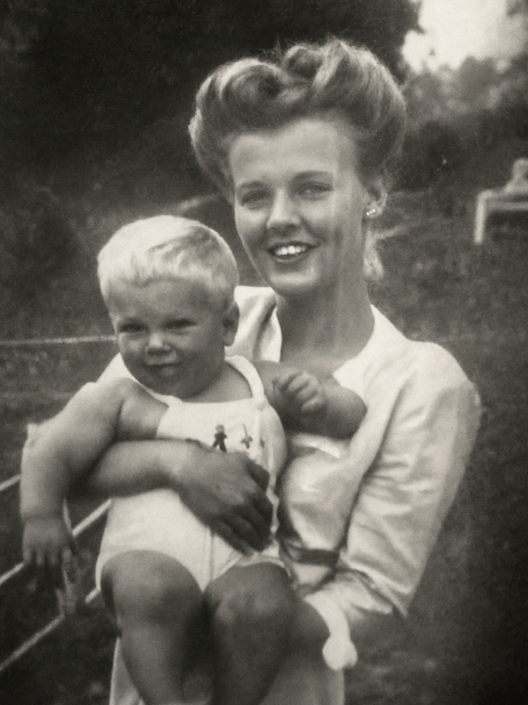Vintage black-and-white photograph of a smiling mother holding young Jack Dell outdoors.